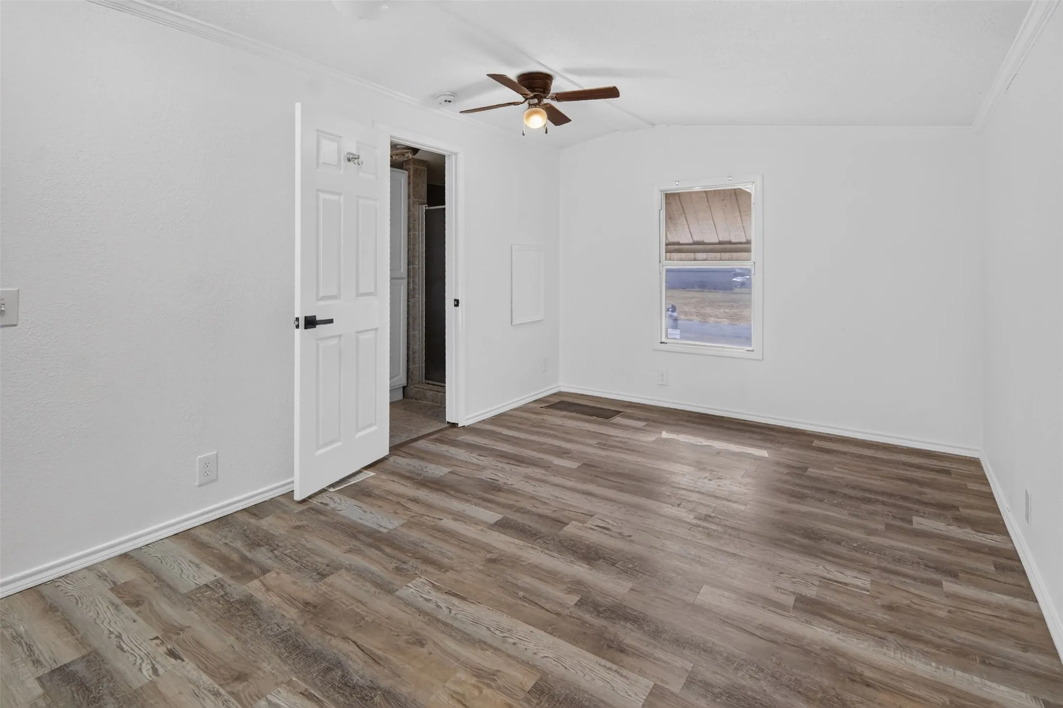 Wood-finish flooring, white walls, ceiling fan, and a window providing natural light