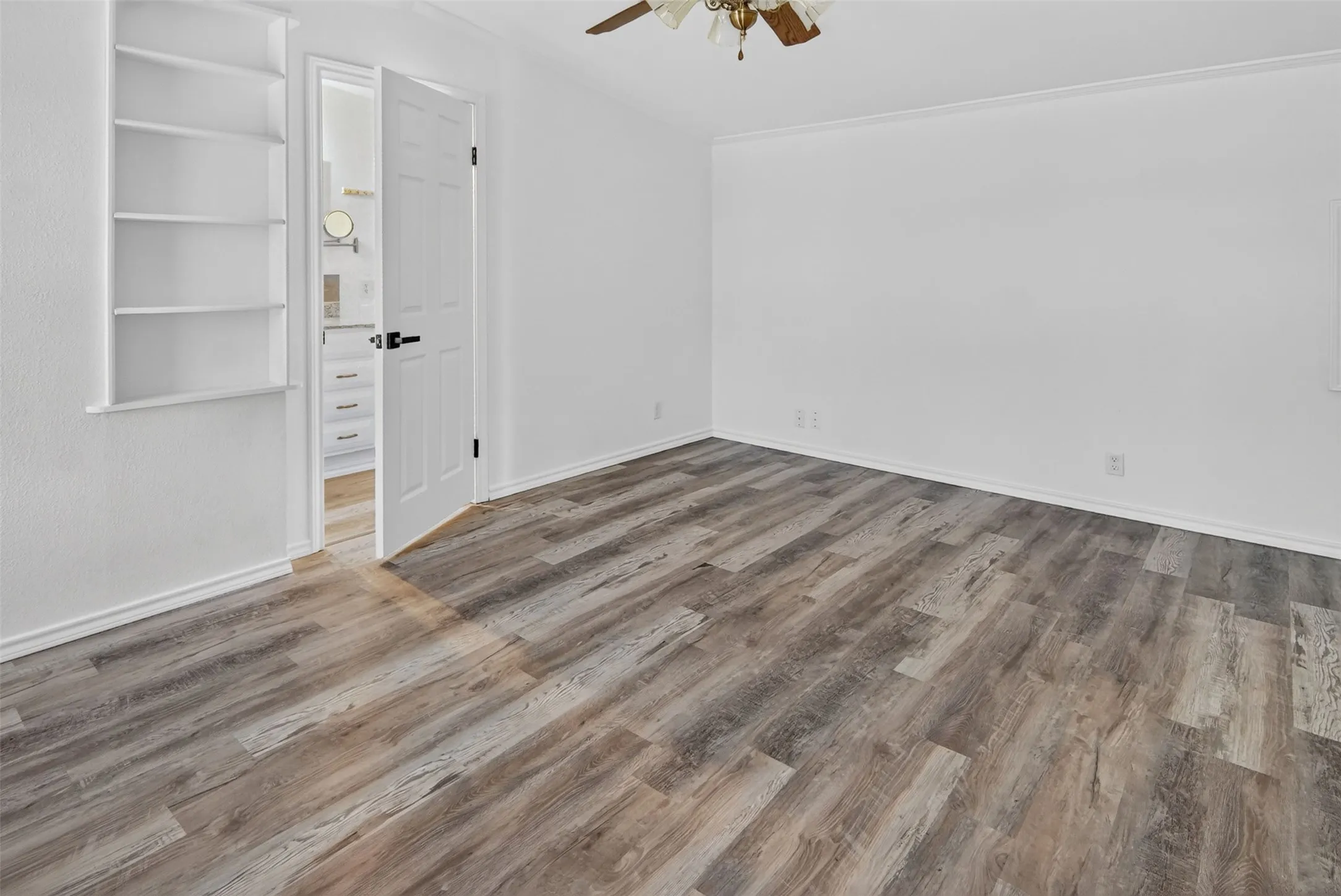 Wood-finish flooring, built-in shelving, white paneled door, ceiling fan, and white walls