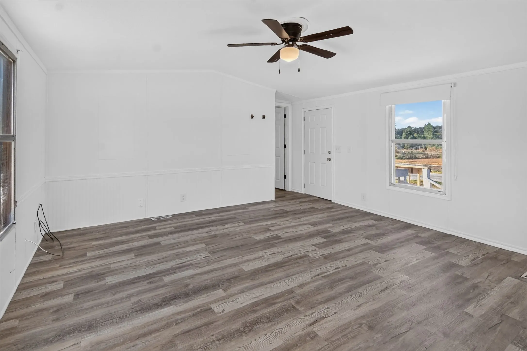 Wood-finish flooring, white paneled wainscoting, white walls, ceiling fan with light fixture, and multiple windows