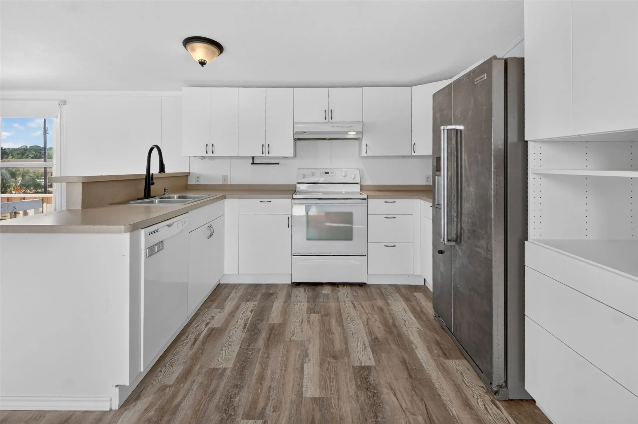 Kitchen featuring white cabinetry, light countertops, wood-finish flooring, stainless steel refrigerator, and white range
