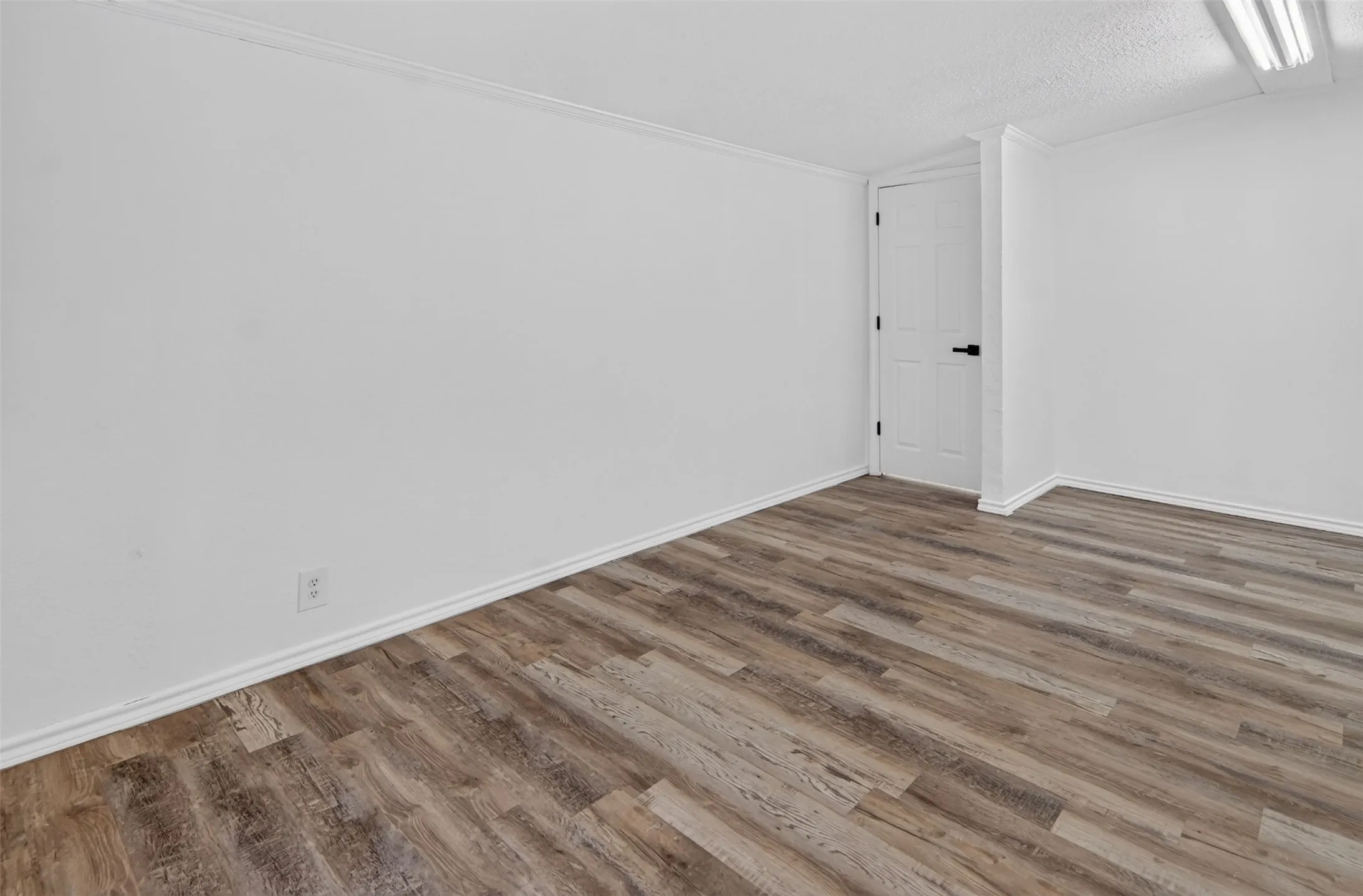 Wood-finish flooring with white baseboards, white walls, and a white paneled door with black hardware