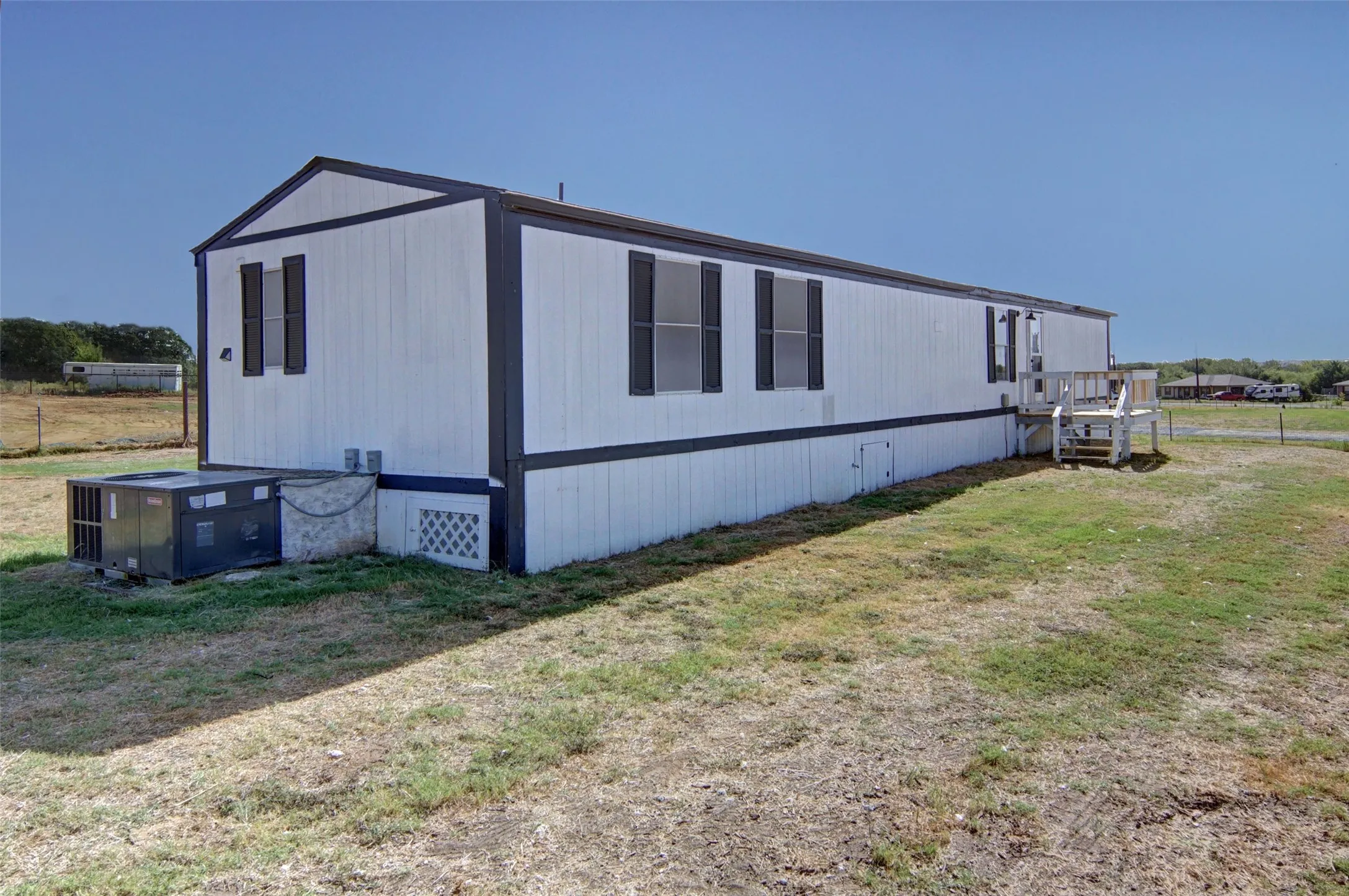 White vertical siding exterior with dark trim, featuring dark window shutters, an exterior deck, and an outdoor air conditioning unit