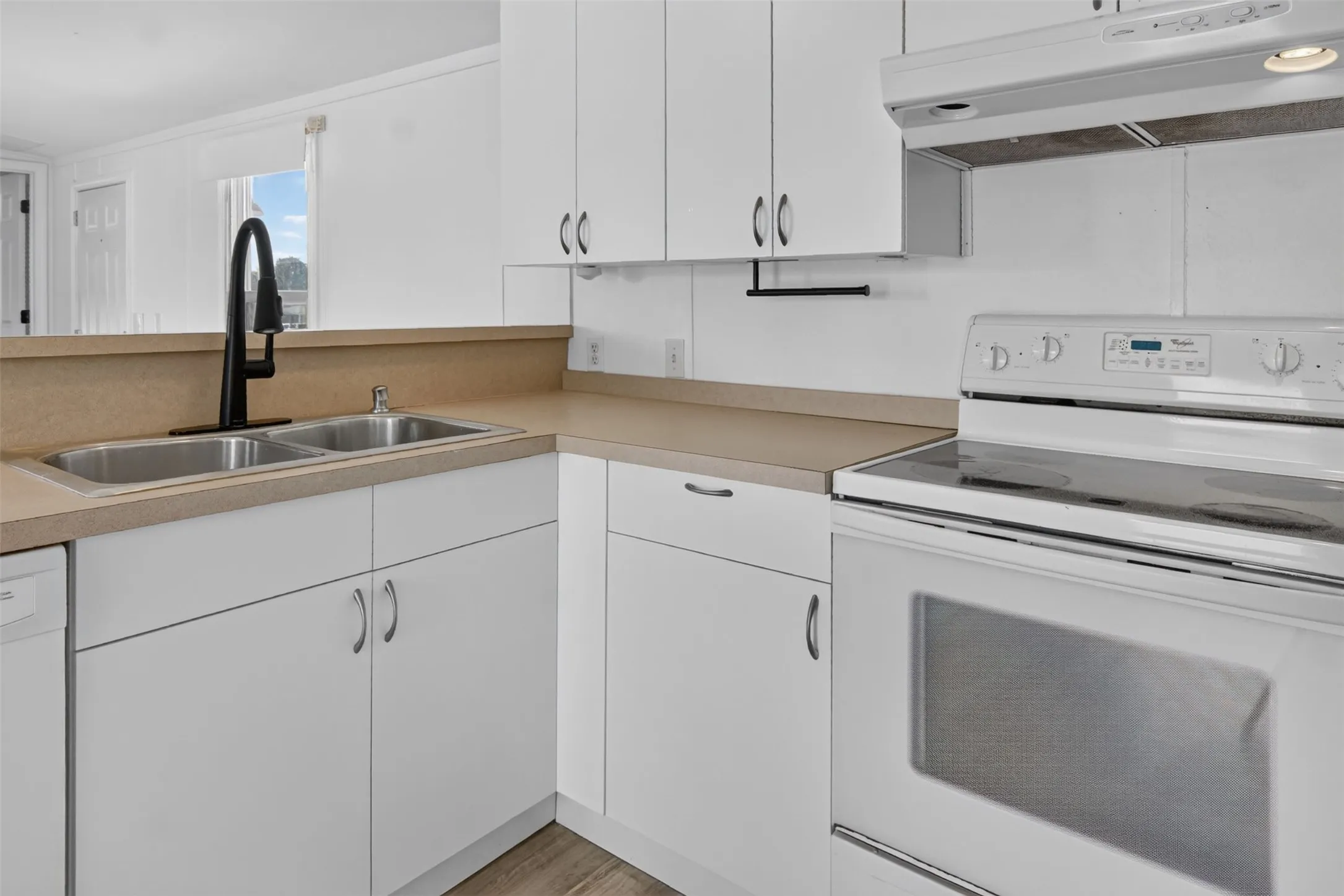 Kitchen featuring white cabinetry, light-toned countertops, a dual basin stainless steel sink with a matte black faucet, a white electric range, and wood-finish flooring