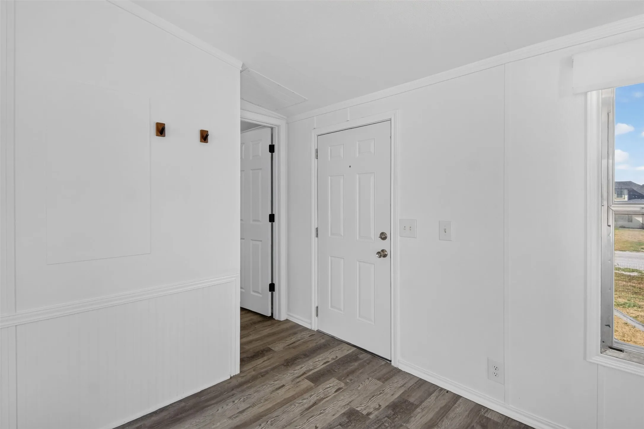 Wood-finish flooring, white paneled walls, white trim, and a white interior door