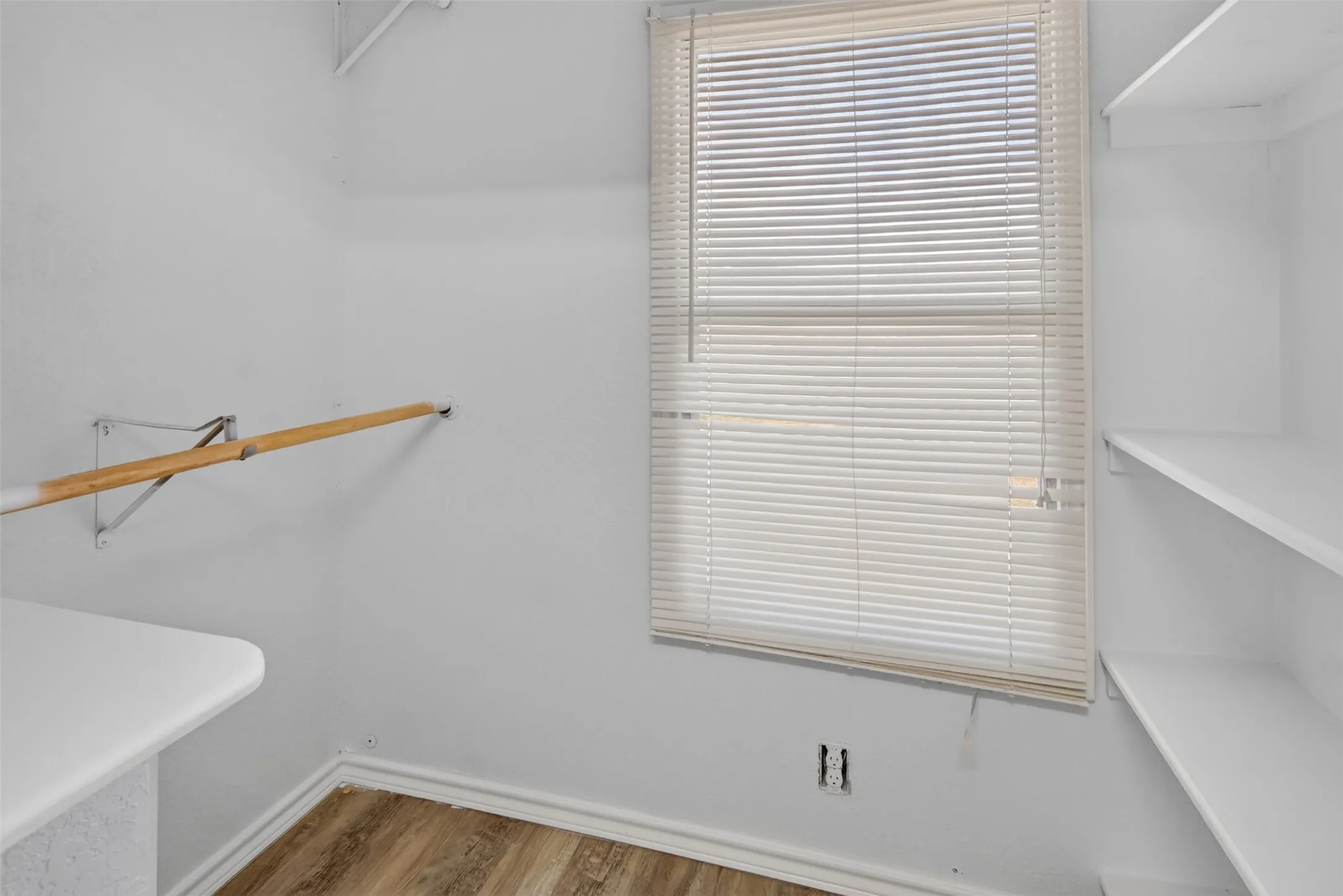 Window with horizontal blinds, built-in shelving, wood-finish flooring, and a wall-mounted folding counter