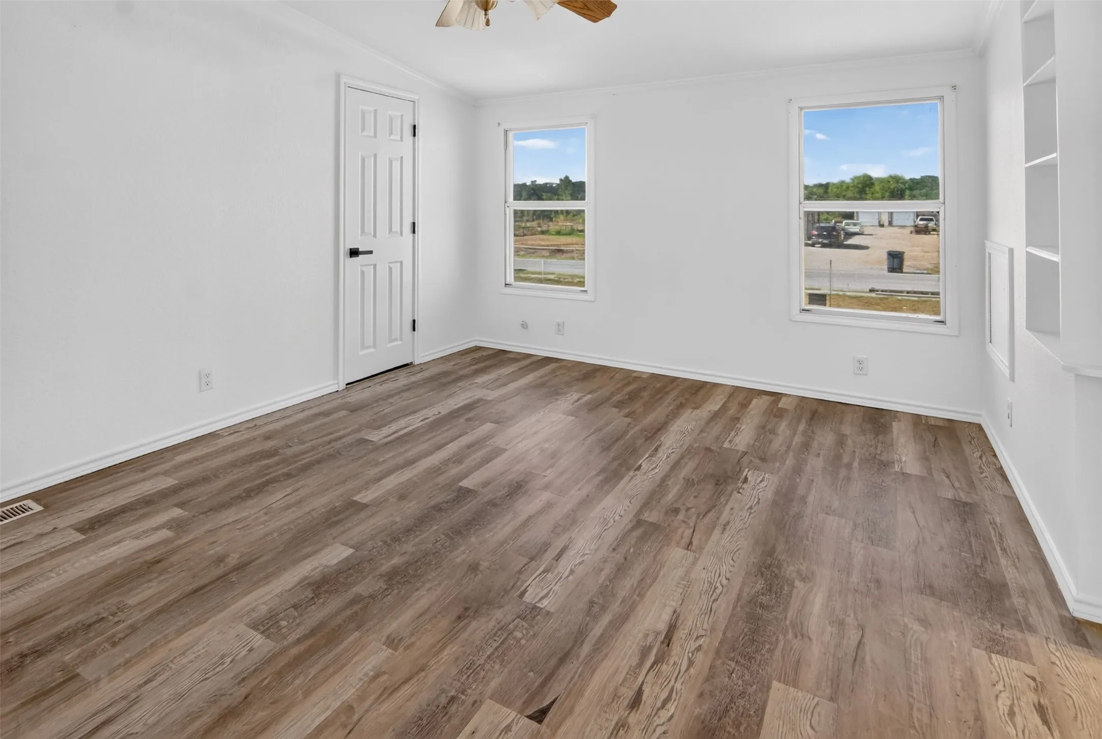 Wood-finish flooring, white paneled door with black hardware, two clear-pane windows, and a built-in shelving unit