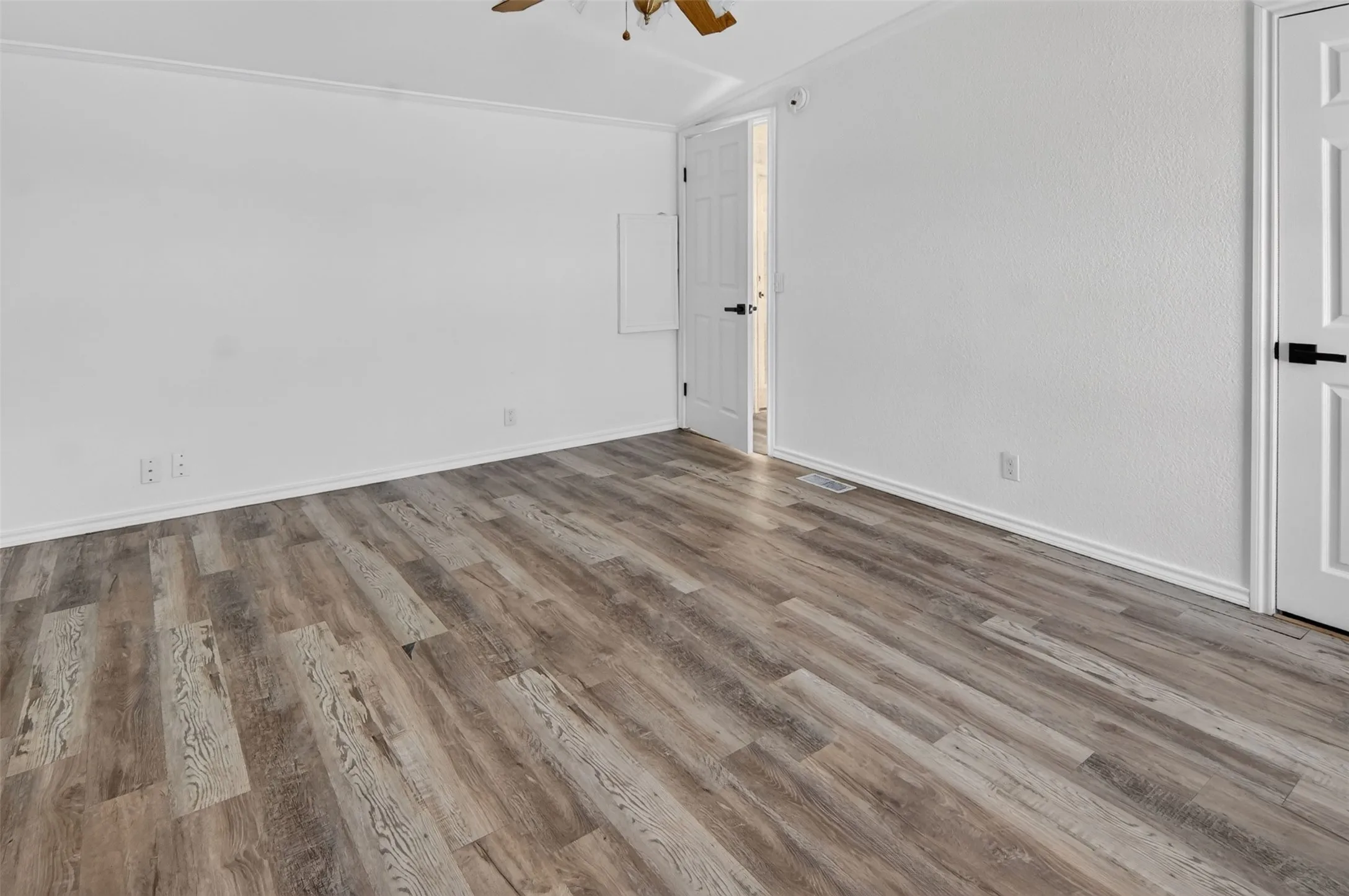 Wood-finish flooring throughout, bright white walls, and a white interior door with black hardware