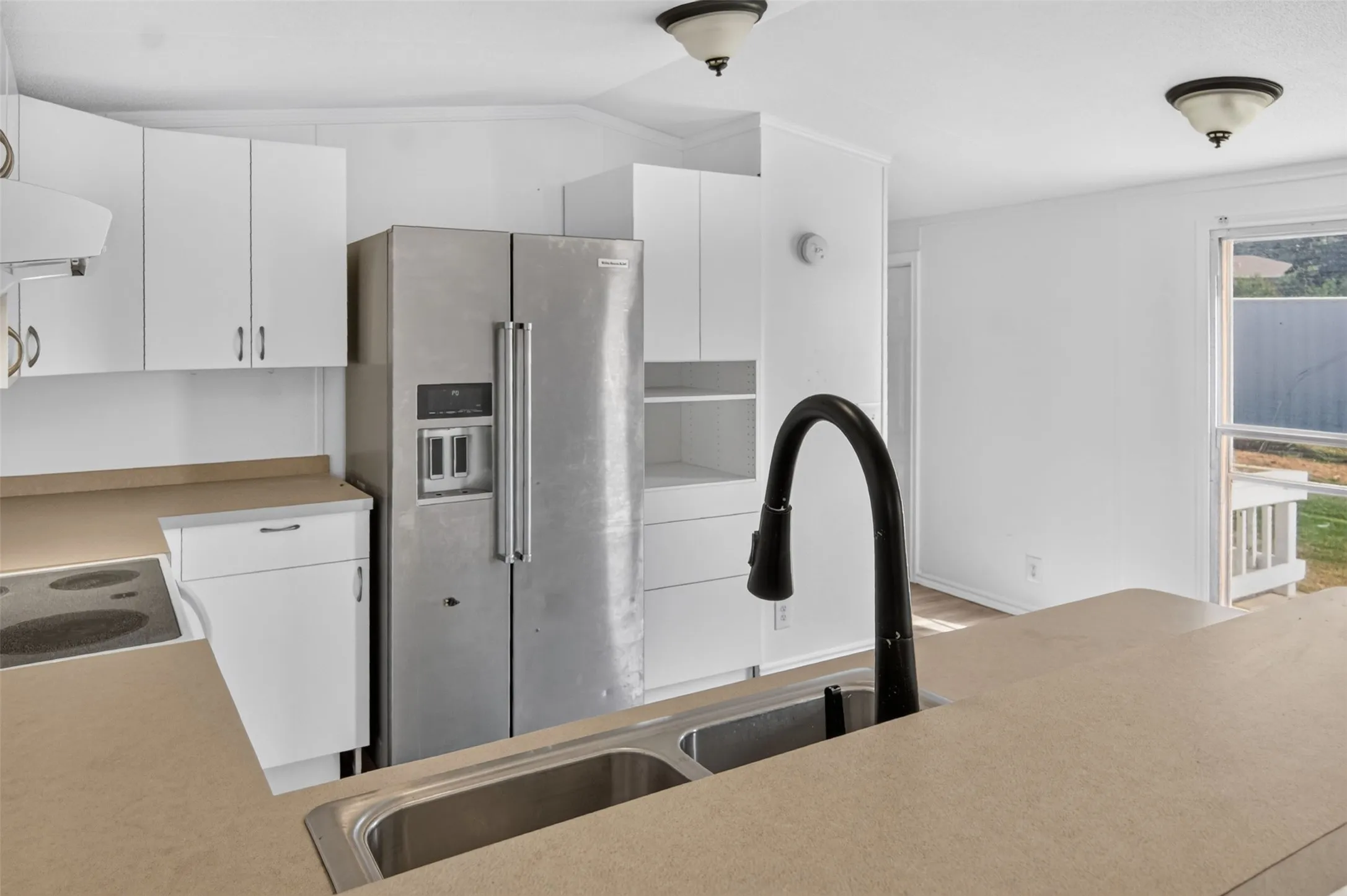 Kitchen featuring white cabinetry, light-toned countertops, a stainless steel refrigerator, a built-in electric stovetop, and a double basin sink with a gooseneck faucet
