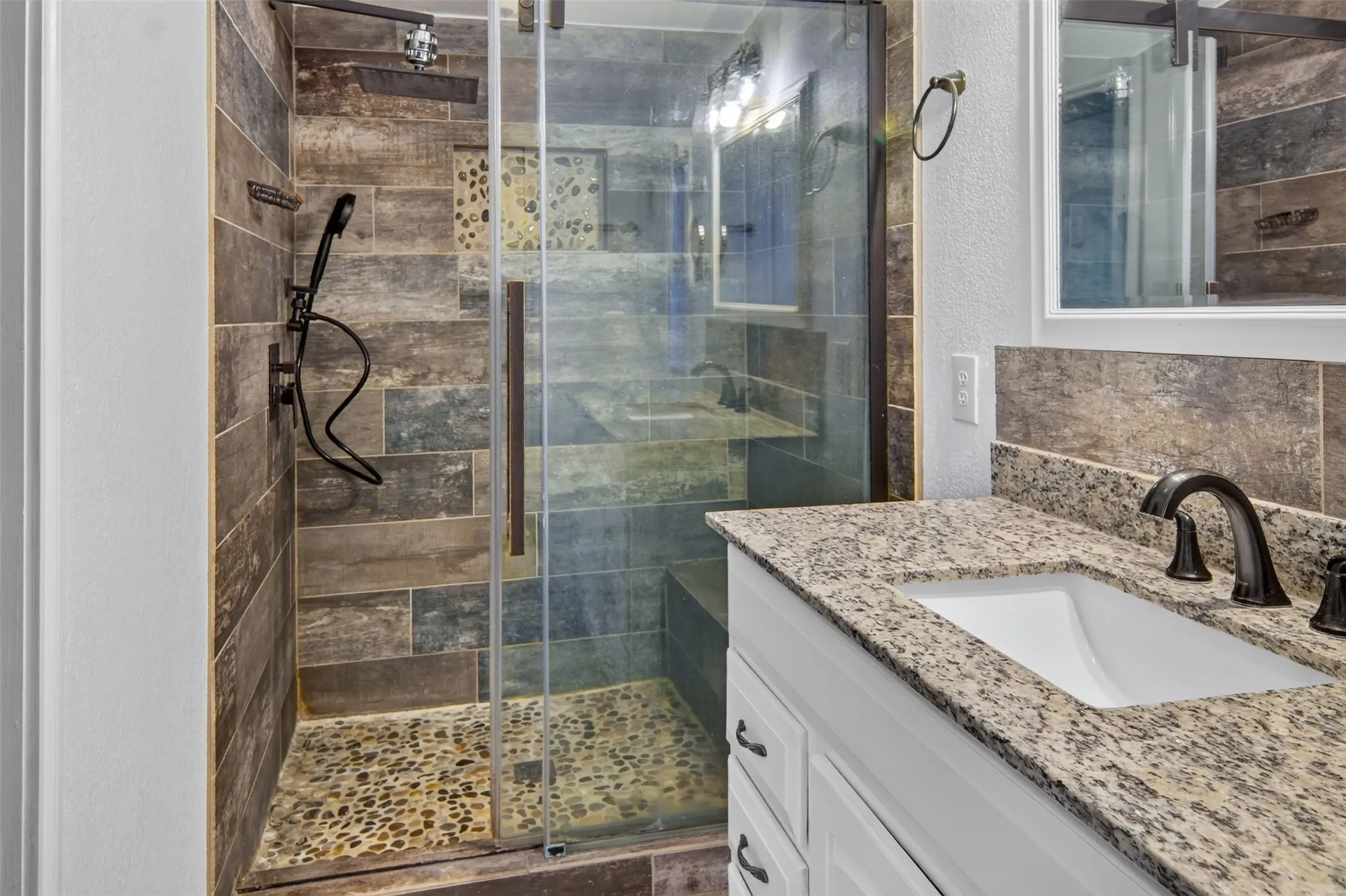 Glass-enclosed shower with pebble-finish flooring, wood-look tile surround, and a built-in shower bench