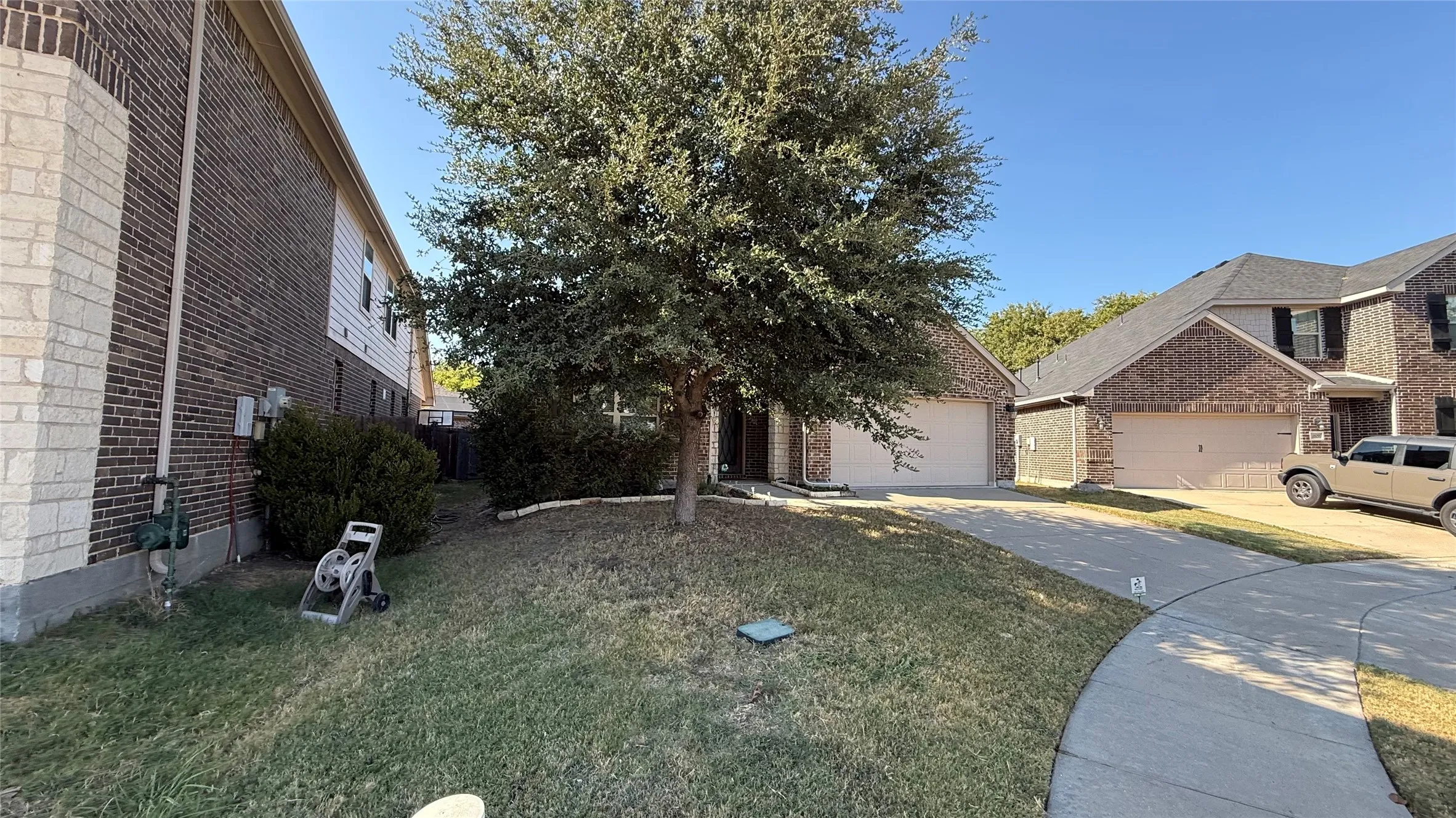 Brick exterior with light-colored accent stone, two-car garage, mature front yard tree, and paved driveway