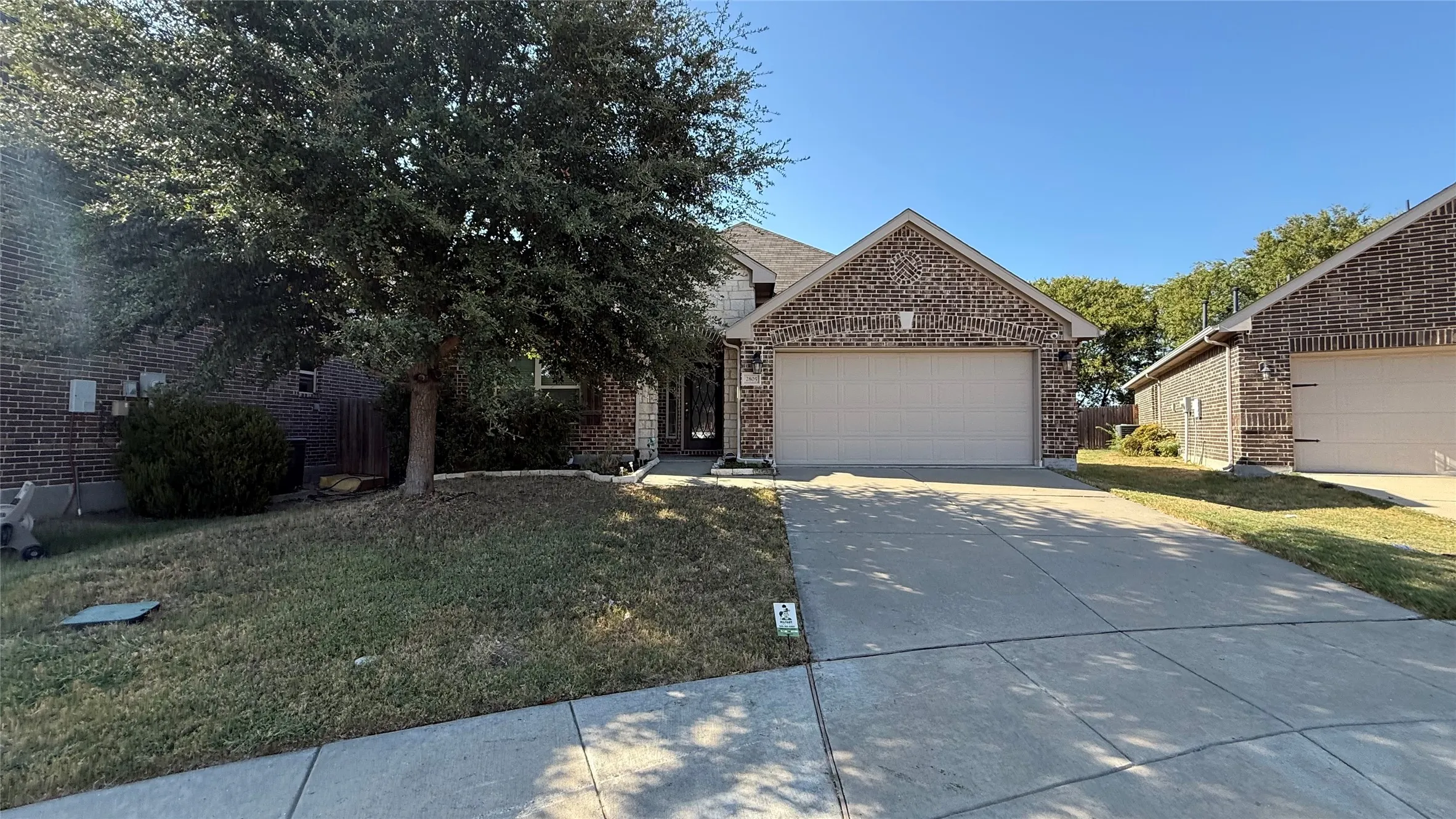 Brick exterior with an attached two-car garage, concrete driveway, and mature landscaping