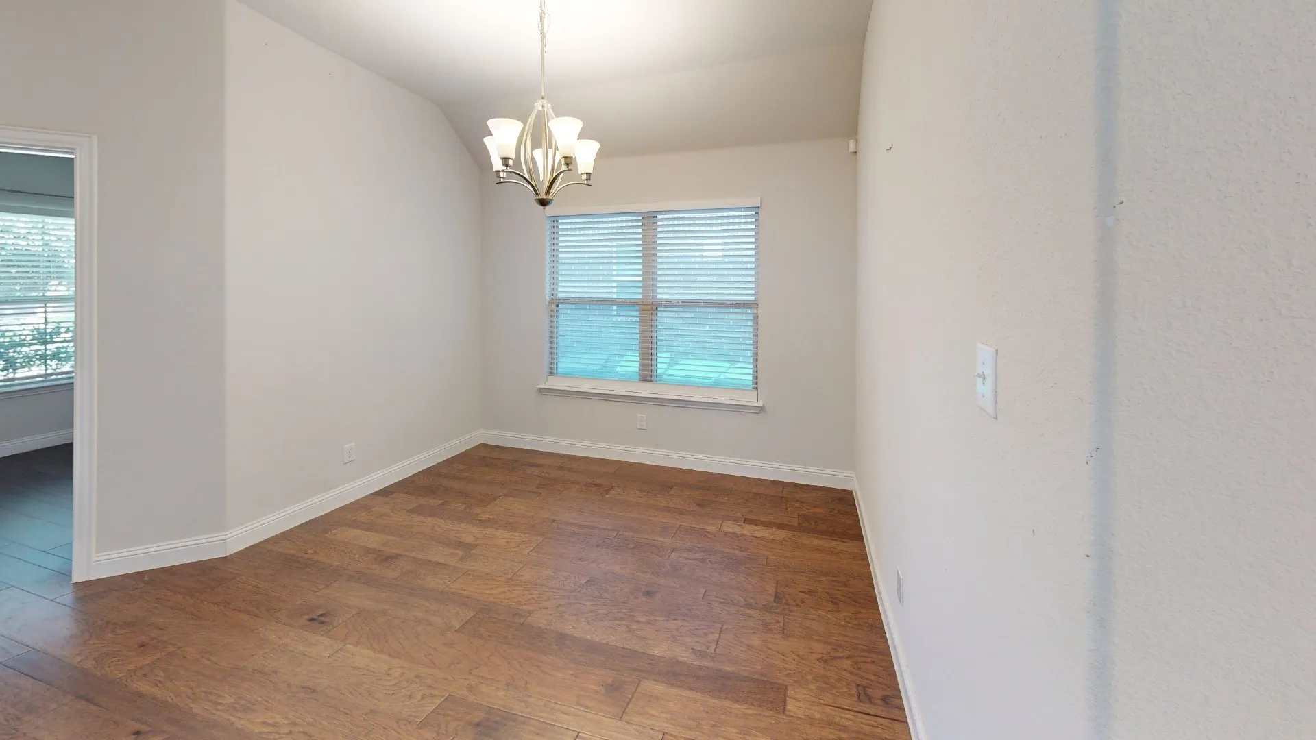 Wood-finish flooring, single window with blinds, and a five-light chandelier