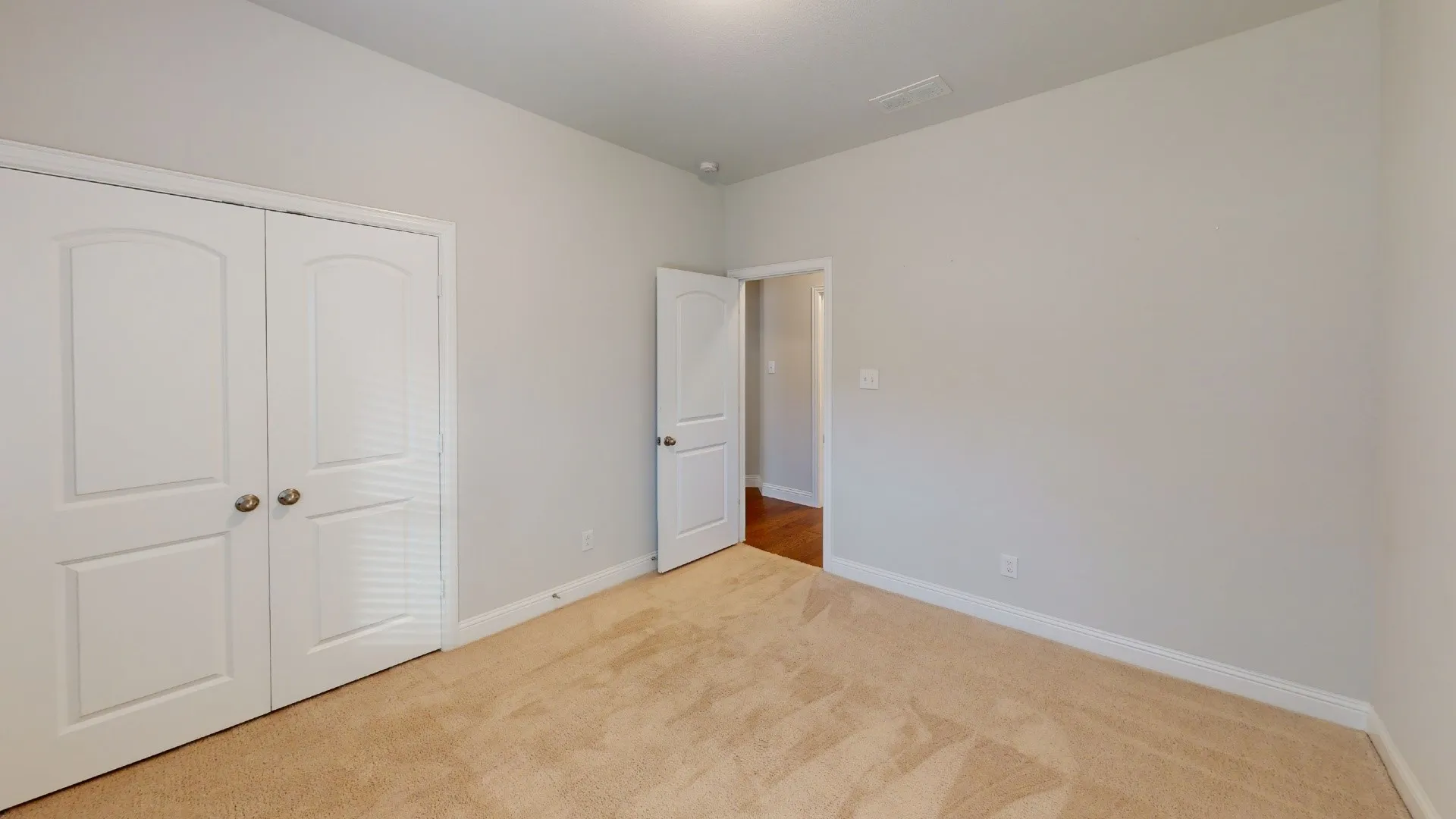 Neutral painted walls, carpet flooring, a white interior door, and a double-door closet with arch-top panels