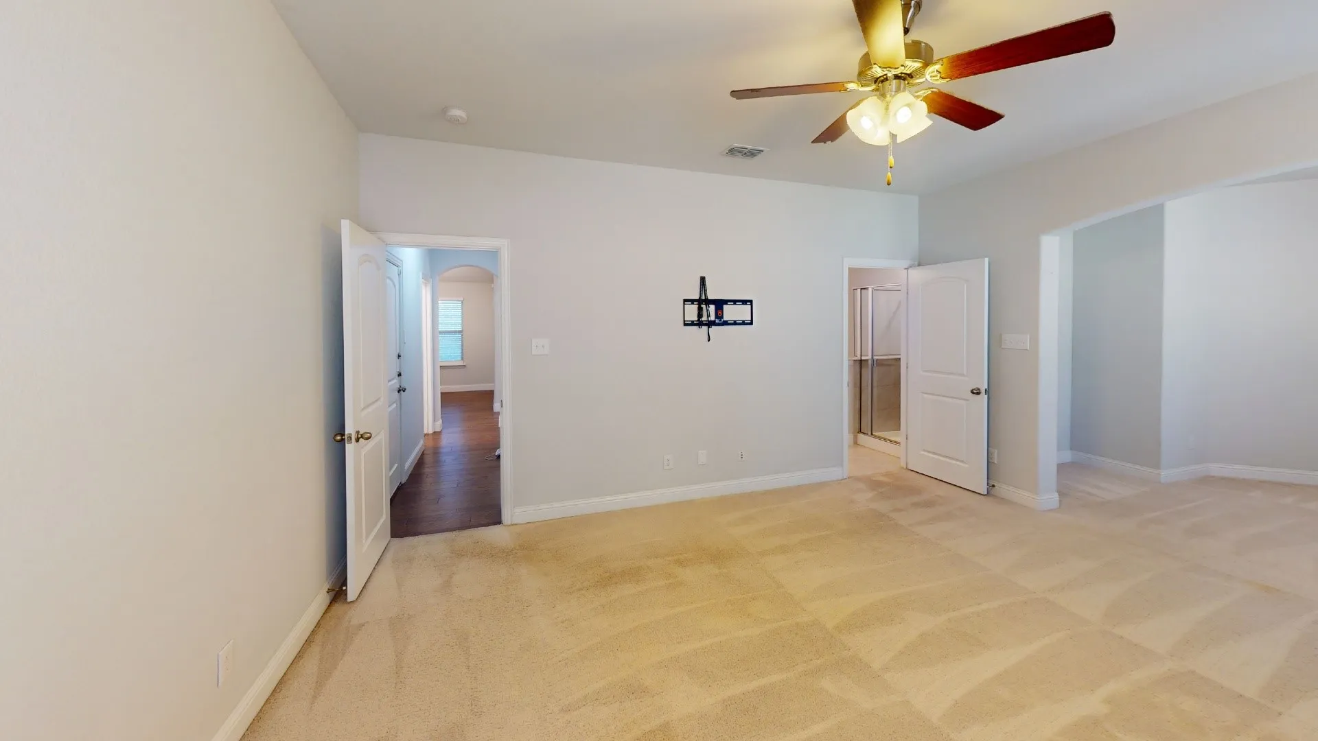 Spacious room with light-colored carpet, a ceiling fan with light fixture, and multiple doorways