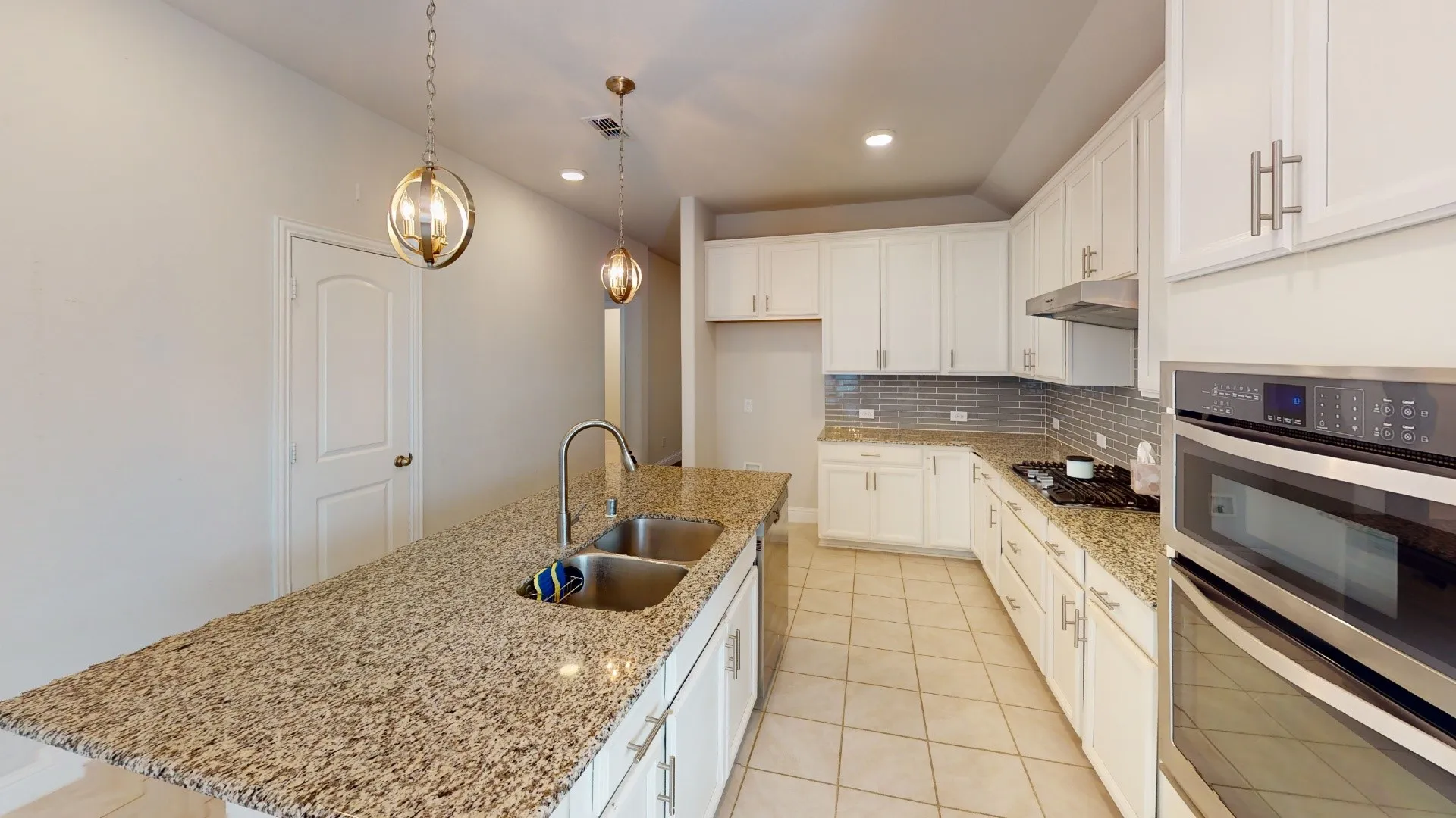Kitchen featuring an island with dual basin sink, integrated wall oven, cooktop, white cabinetry, and granite countertops