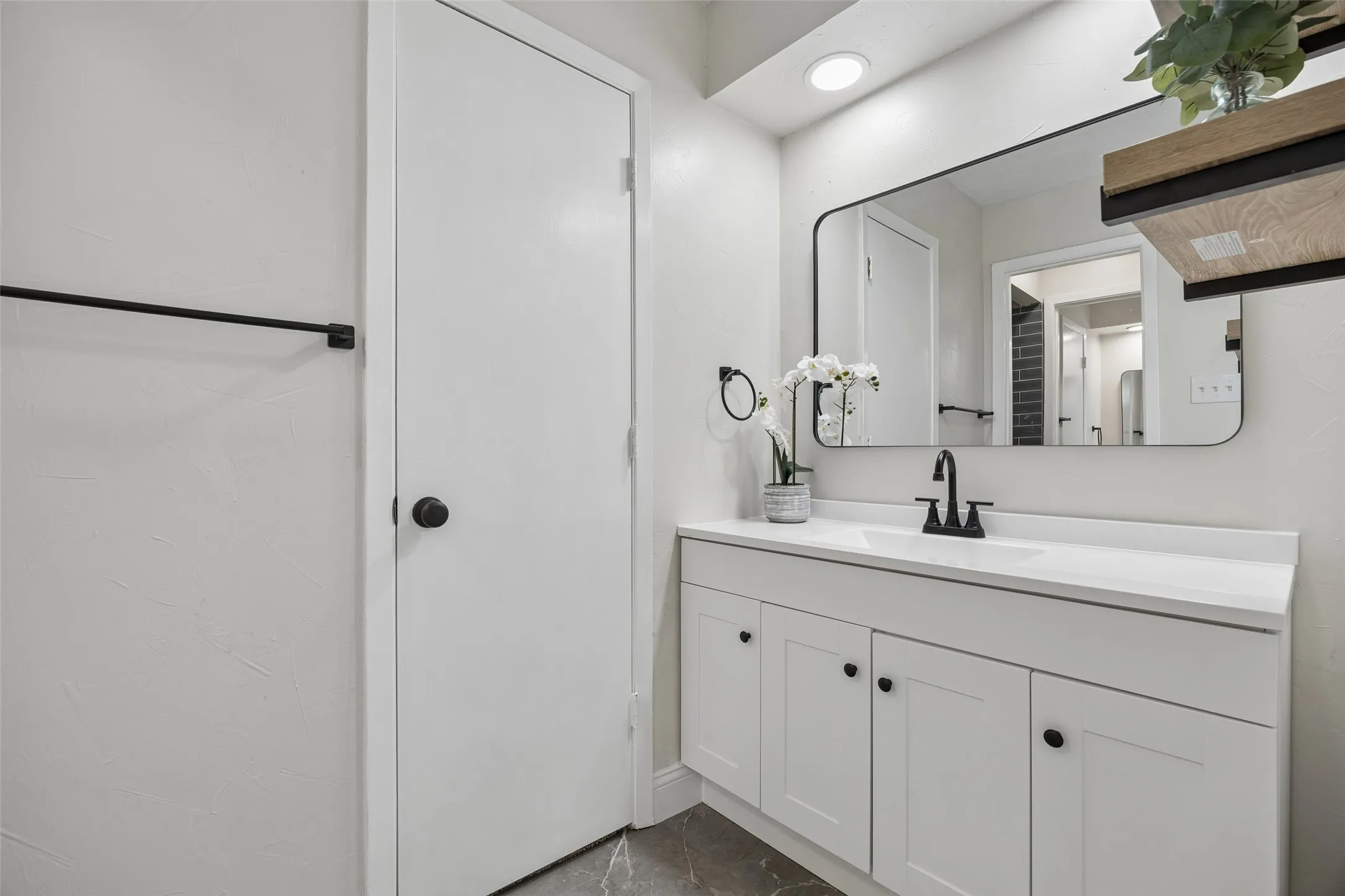 White vanity with matte black hardware, white countertop, rectangular framed mirror, and recessed lighting