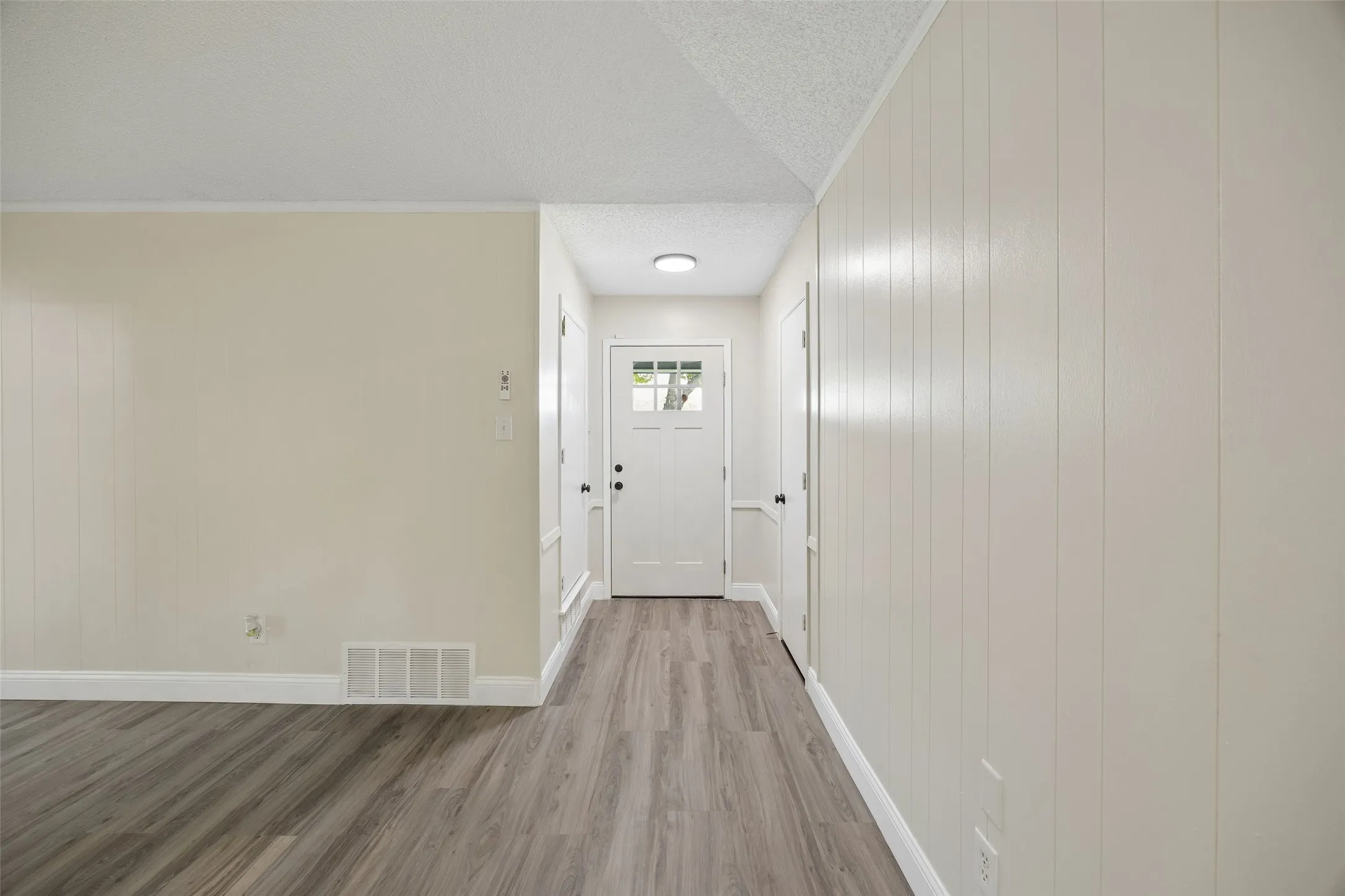 Wood-finish flooring, white paneling, white interior doors, and a front entry door with glass inserts