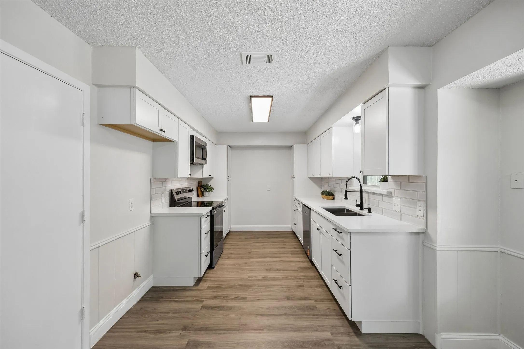 Galley kitchen featuring white cabinetry, quartz countertops, subway tile backsplash, and wood-finish flooring