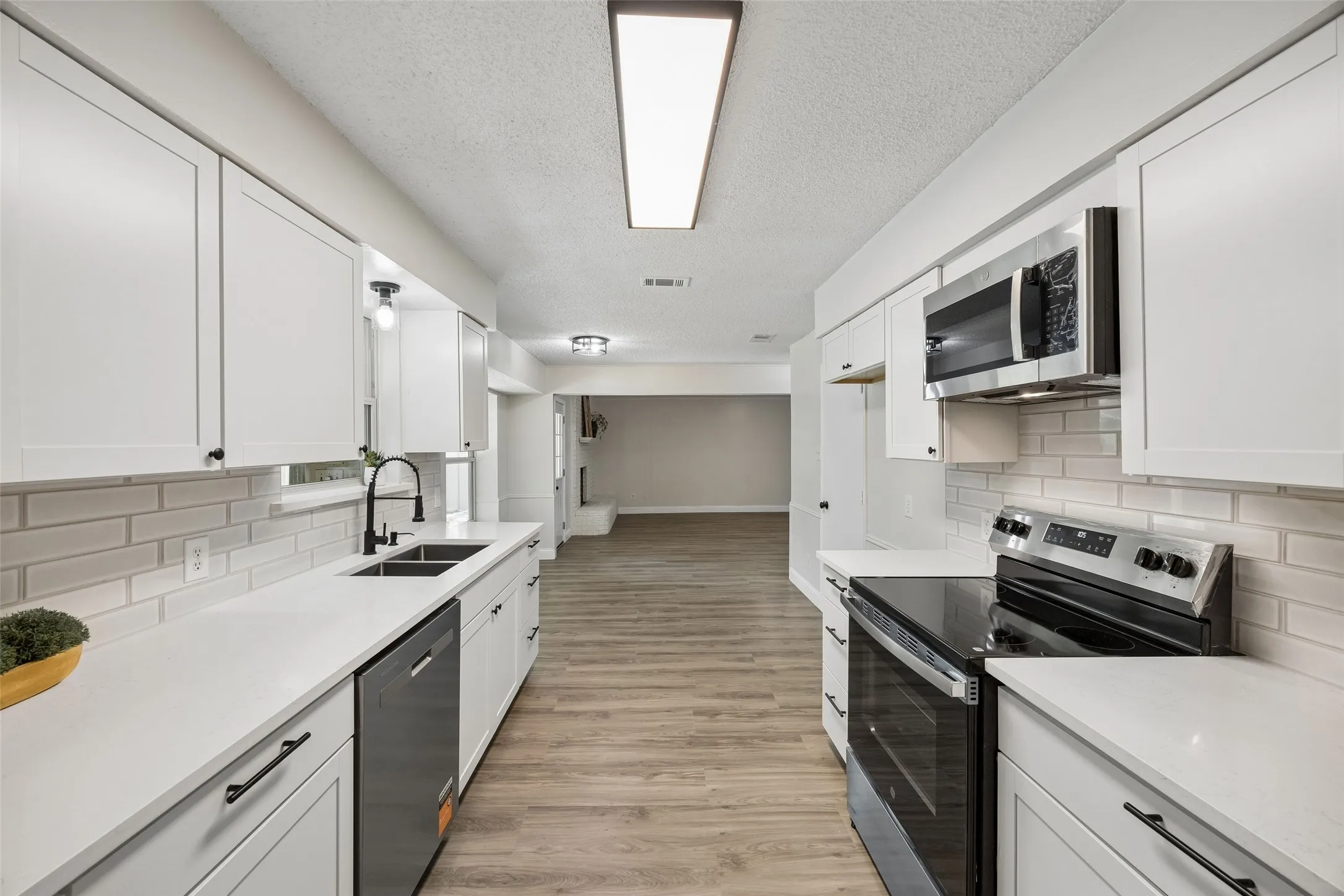 Galley kitchen featuring white cabinetry, quartz countertops, subway tile backsplash, stainless steel appliances, and wood-finish flooring
