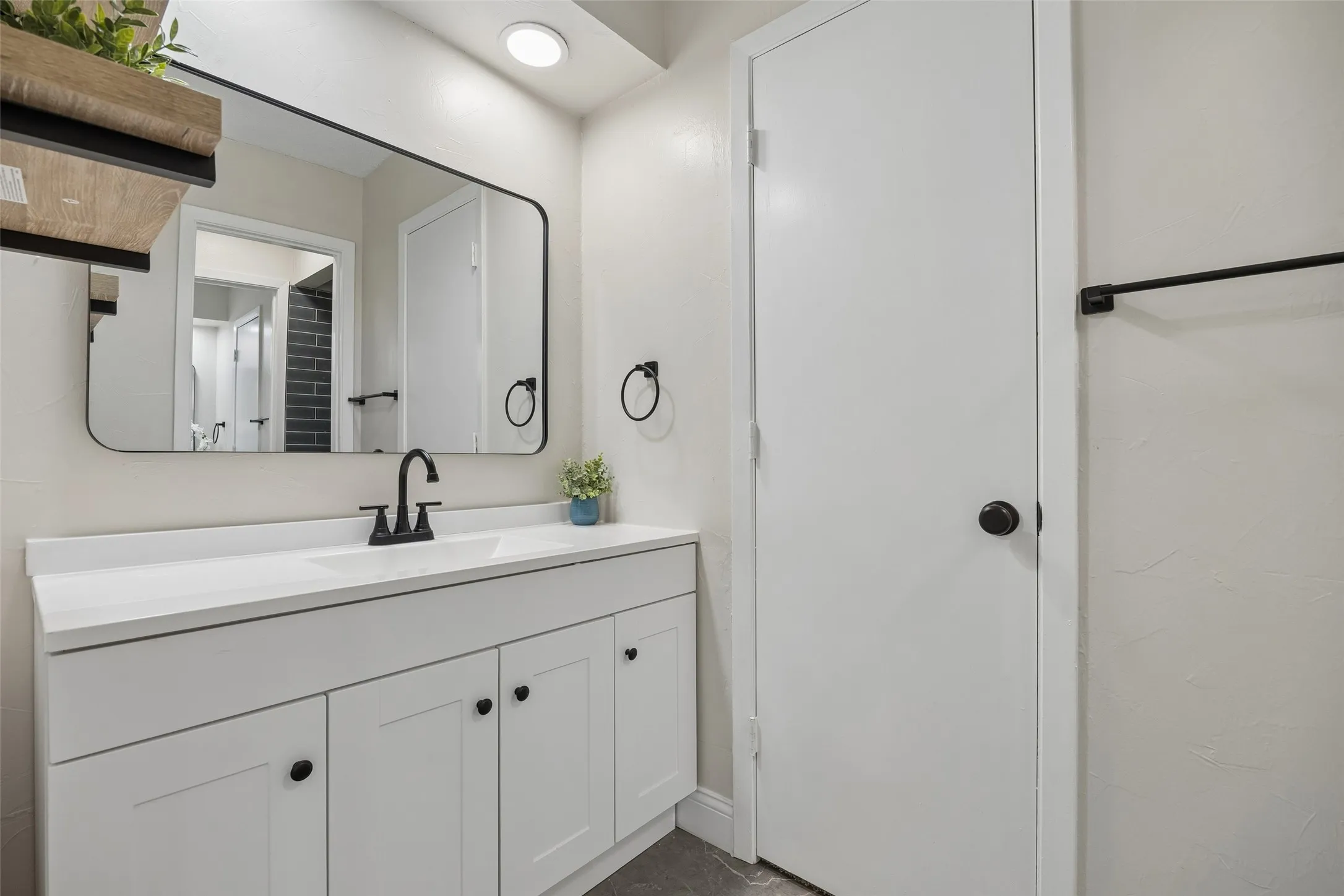 White vanity with shaker-style cabinetry, matte black hardware, integrated sink, and wall-mounted mirror