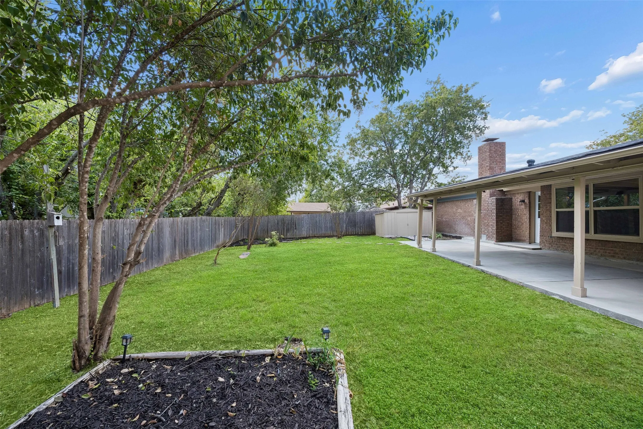 Expansive backyard featuring a manicured lawn, established perimeter fencing, and a covered concrete patio