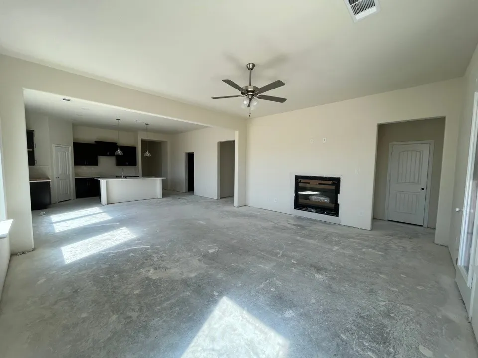 Open-concept living area featuring a built-in fireplace, ceiling fan, and access to a kitchen with dark cabinetry, a center island, and pendant lighting