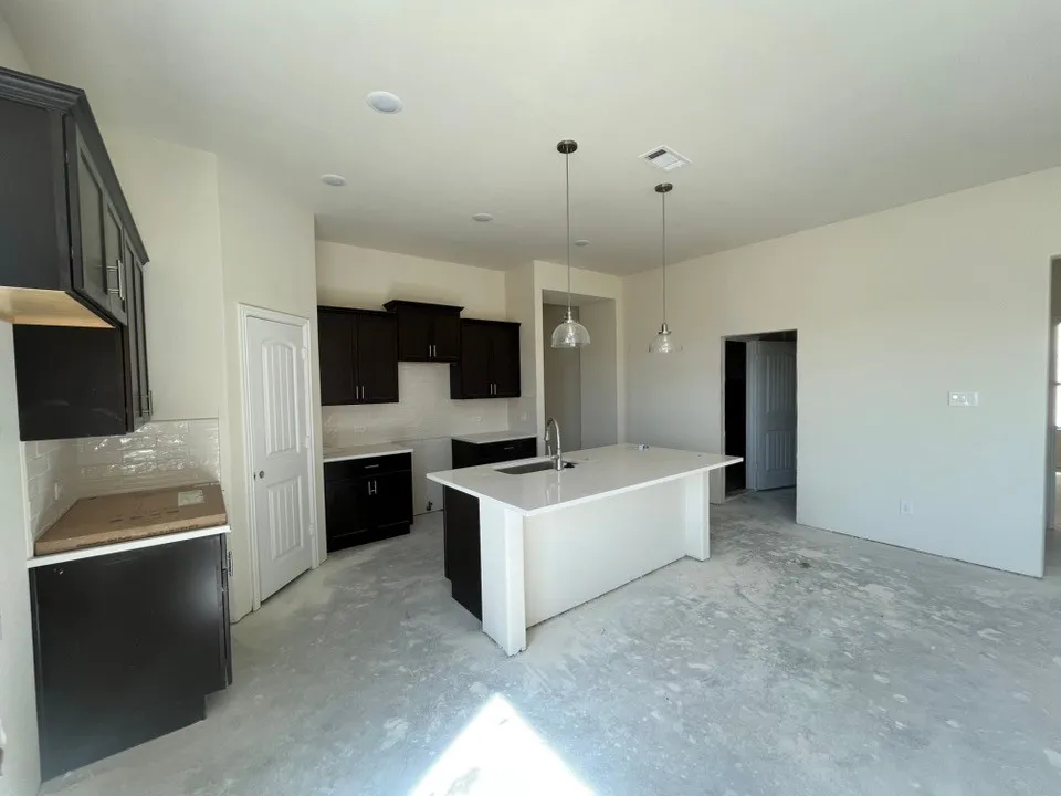 Kitchen featuring dark wood cabinetry, white subway tile backsplash, white island with integrated sink, and pendant lighting