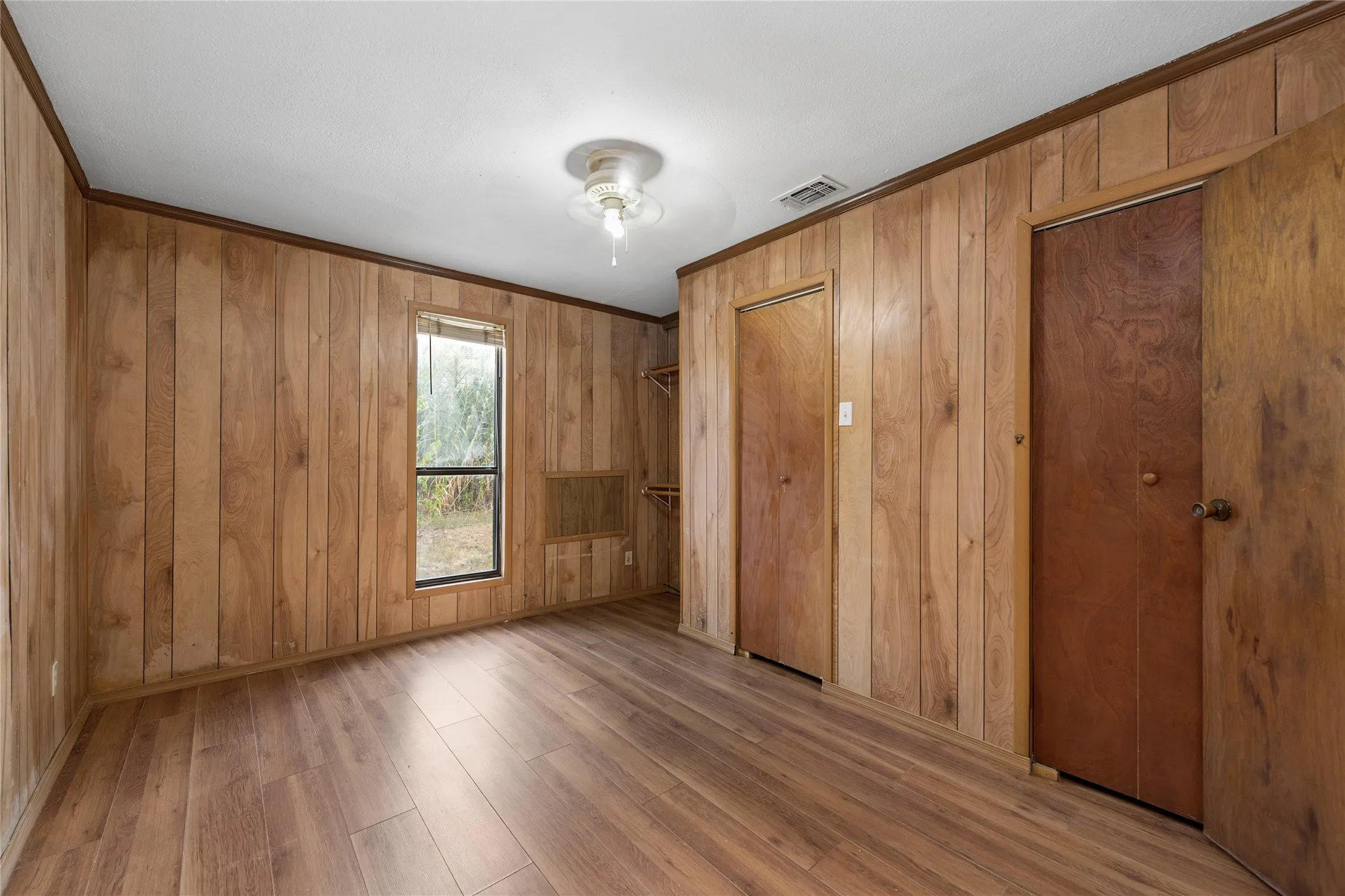 Wood-finish flooring and paneling with a ceiling-mounted light fixture, window, and two wooden doors