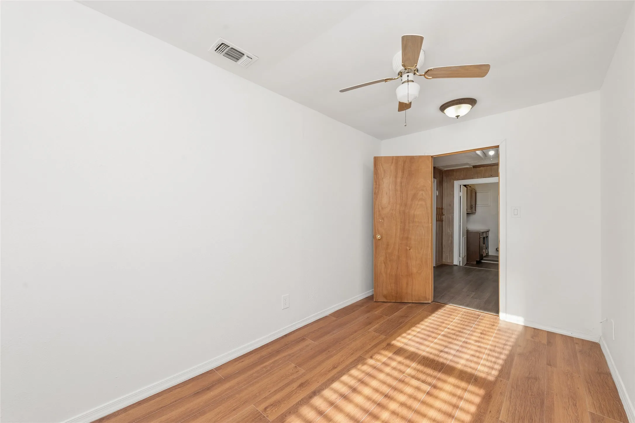 Wood-finish flooring, white painted walls, ceiling fan, flush-mount ceiling light, and a solid wood interior door