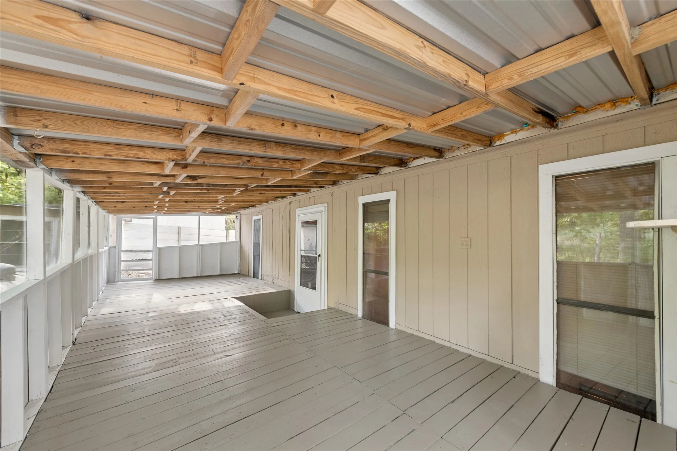 Enclosed porch featuring a metal roof, exposed wood beam ceiling, painted wood flooring, and multiple exterior doors