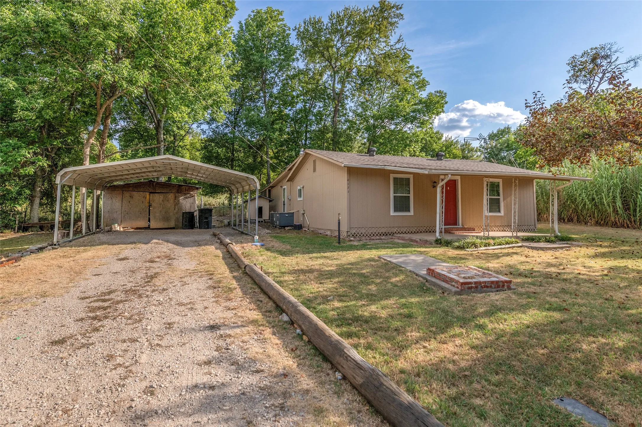Single-story residence with a covered front porch, gravel driveway, and a detached metal carport structure