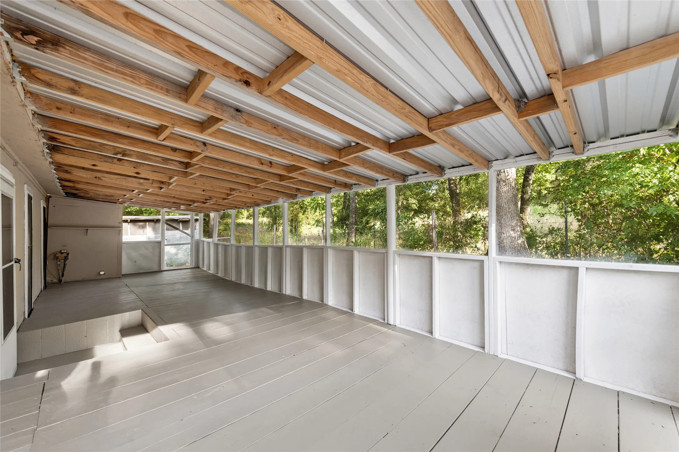 Expansive screened porch with wood-finish flooring, a metal roof, and exposed wood ceiling beams