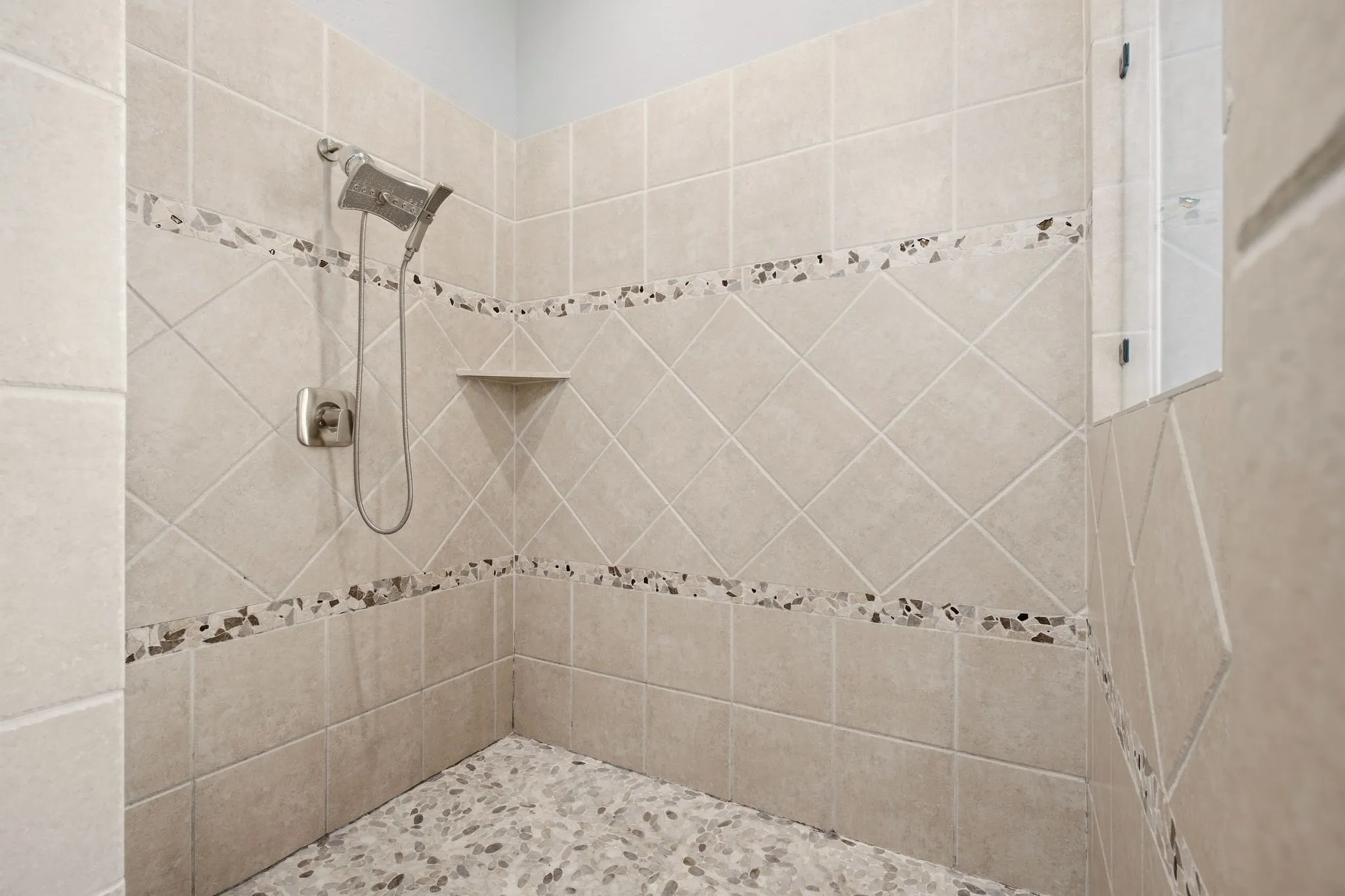 The deep walk-in shower has pebblestone flooring & wall accents.