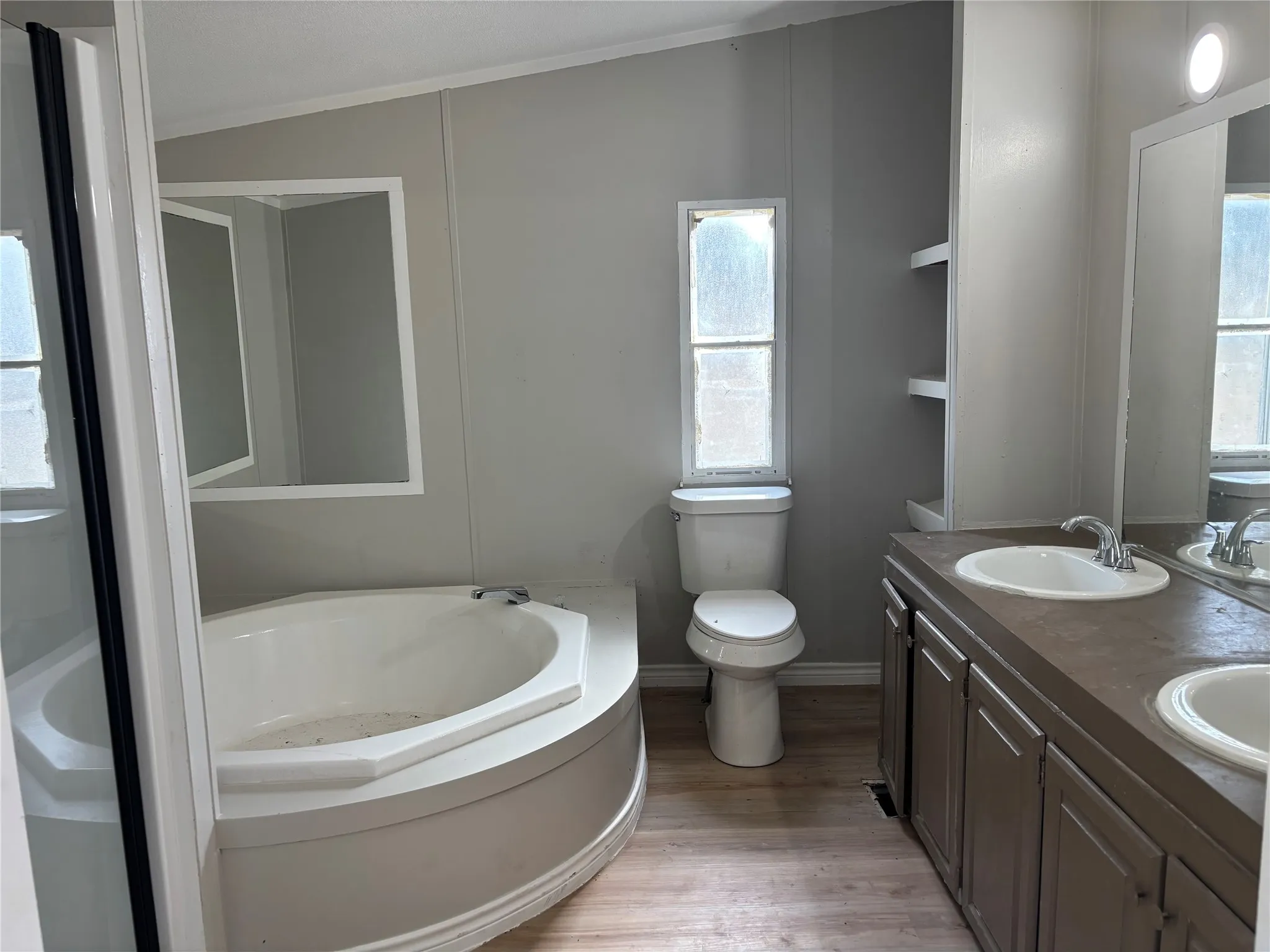 Corner soaking tub, dual vanity with integrated sinks, built-in shelving, and wood-finish flooring