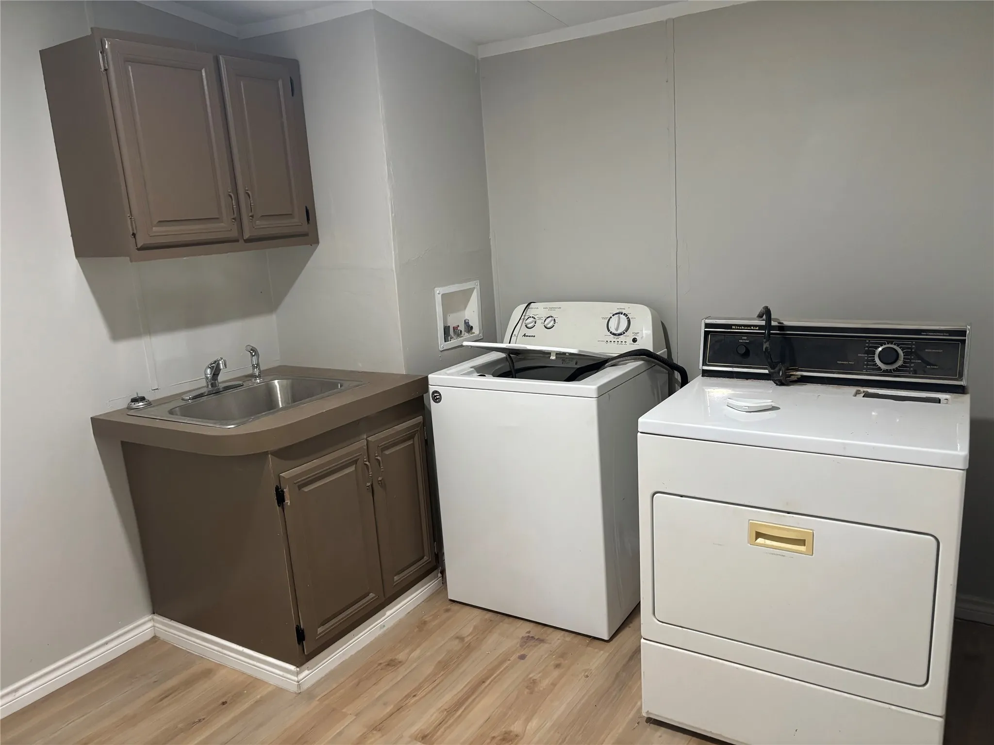 Utility area featuring wood-finish flooring, a stainless steel utility sink, and built-in cabinetry