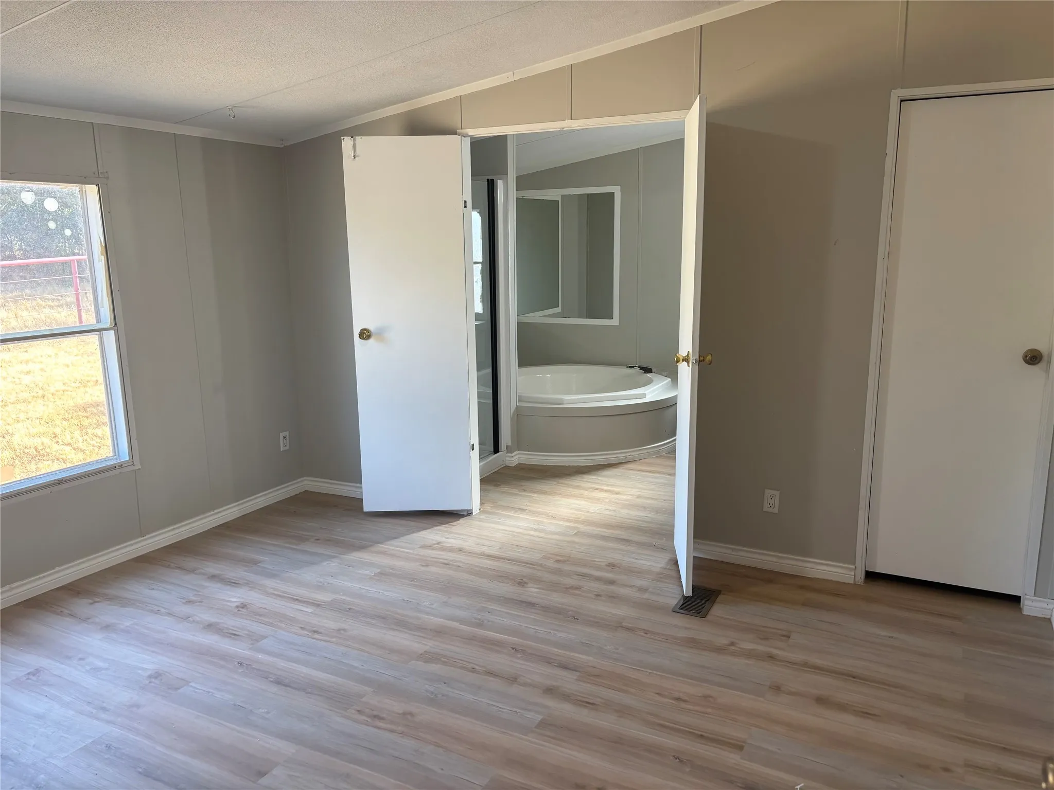 Light wood-finish flooring throughout, neutral wall paint, and a corner window