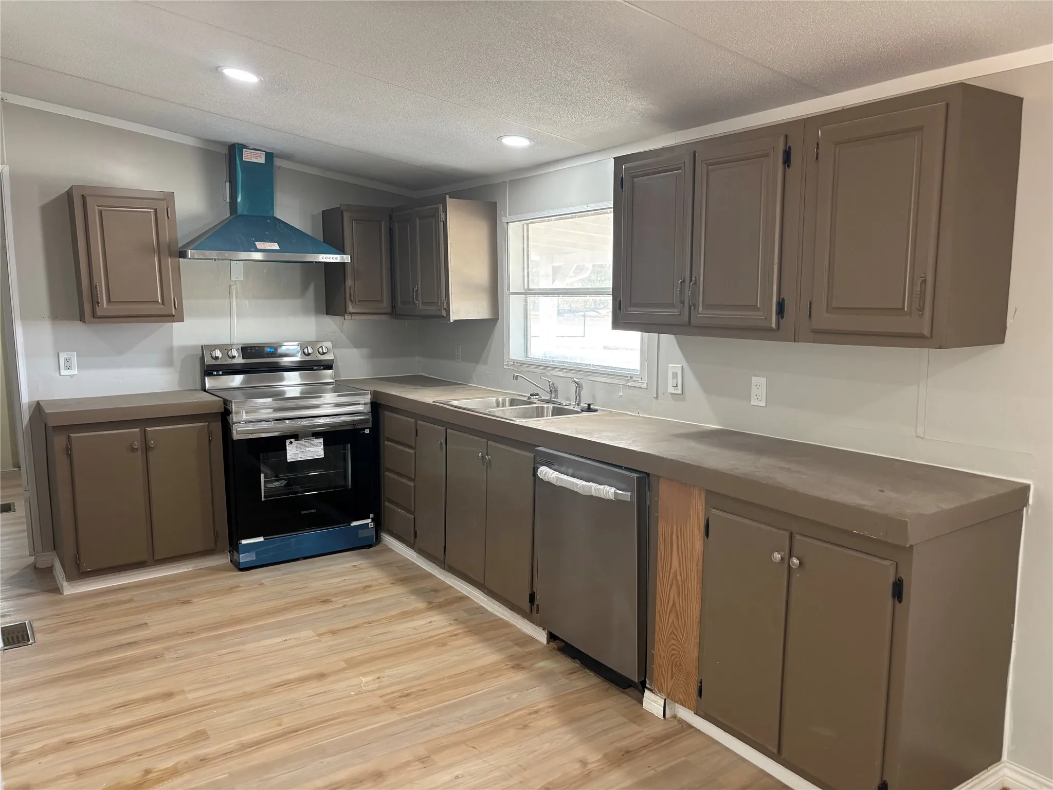 Kitchen featuring new stainless steel appliances, a range hood, wood-finish flooring, and ample cabinet storage