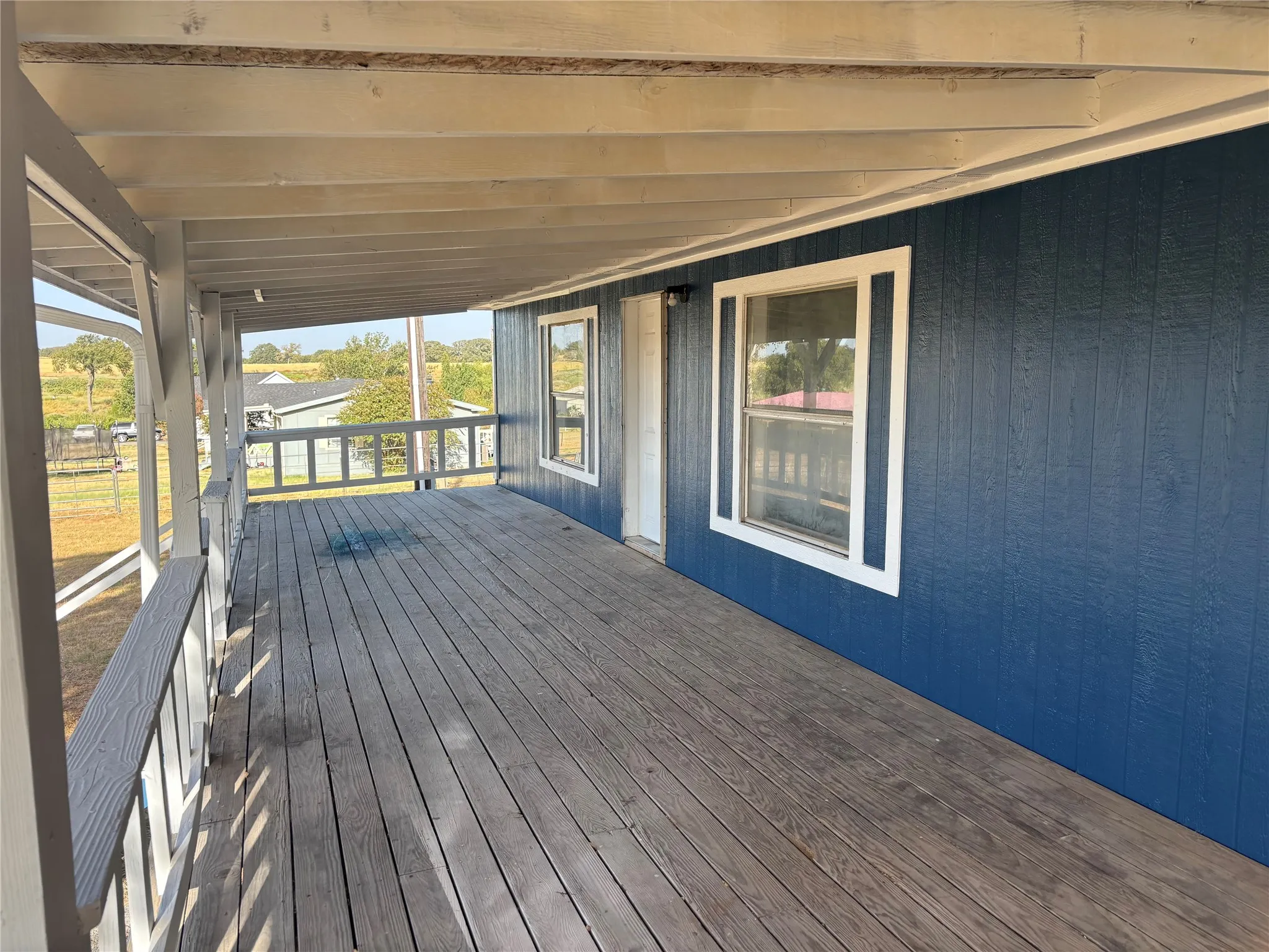 Covered porch featuring a wooden deck, painted blue siding, and white window trim