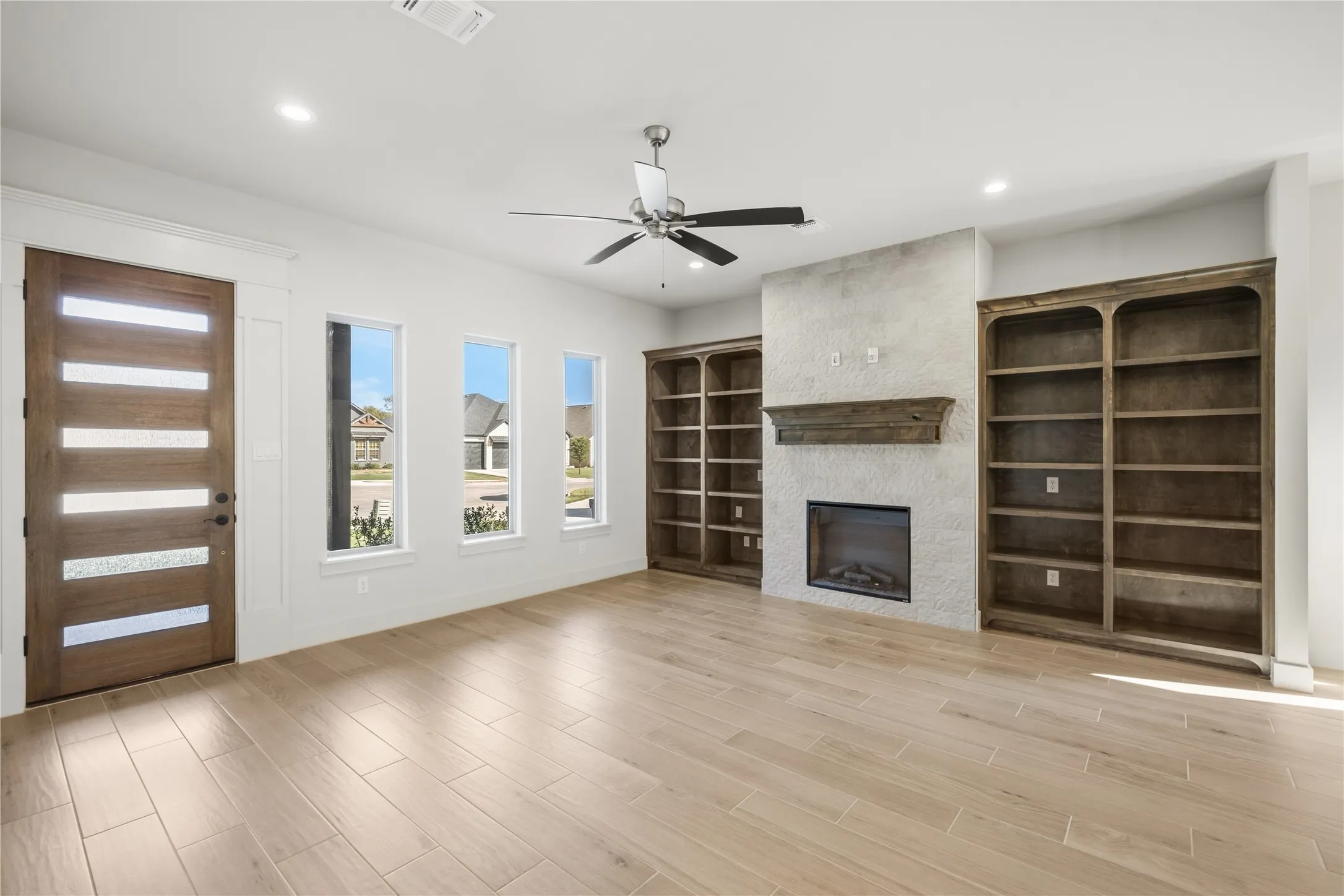 Wood-finish flooring, built-in shelving, fireplace with a wood mantel, and a modern entry door