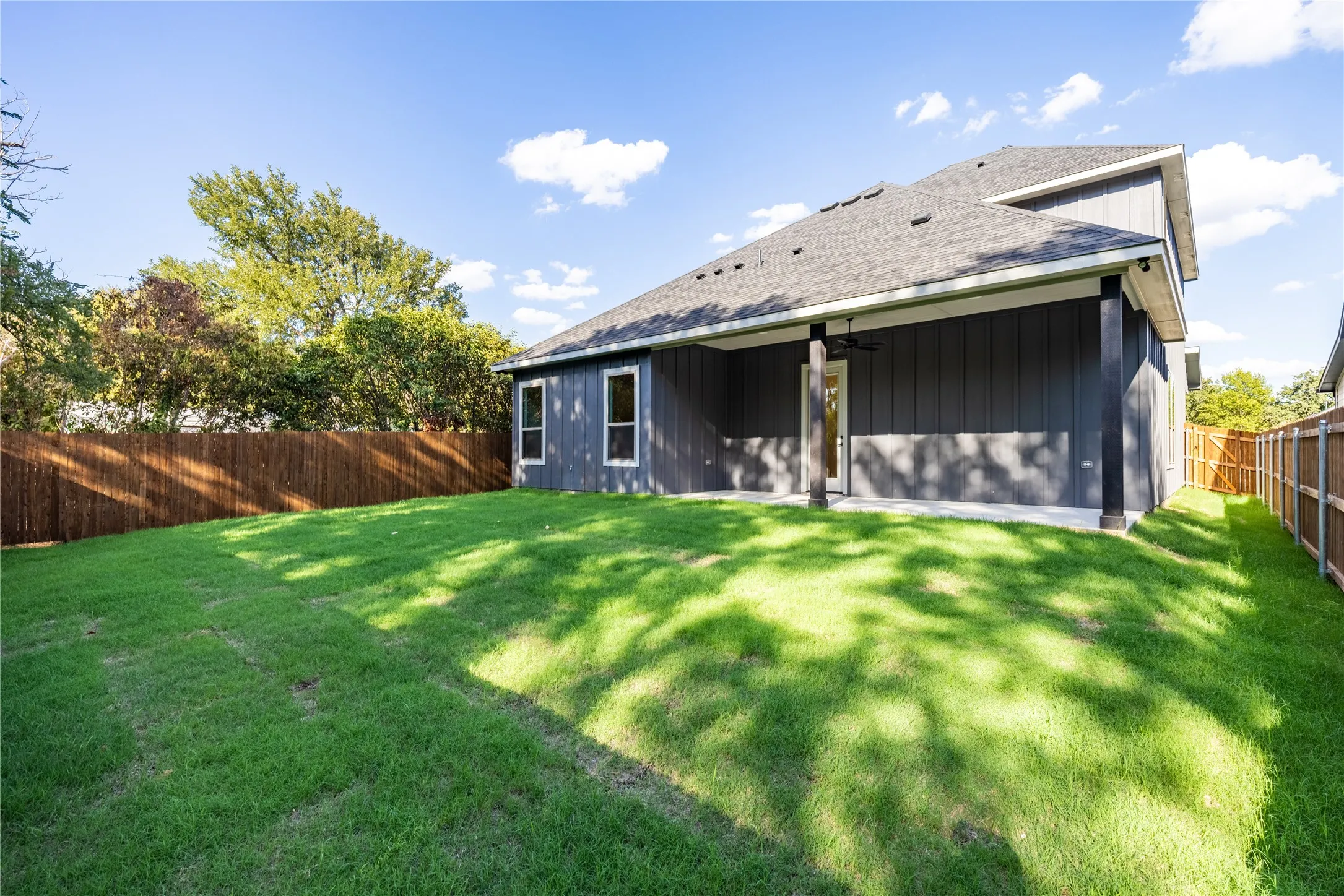Expansive backyard featuring a manicured lawn, wood fencing, and a concrete patio