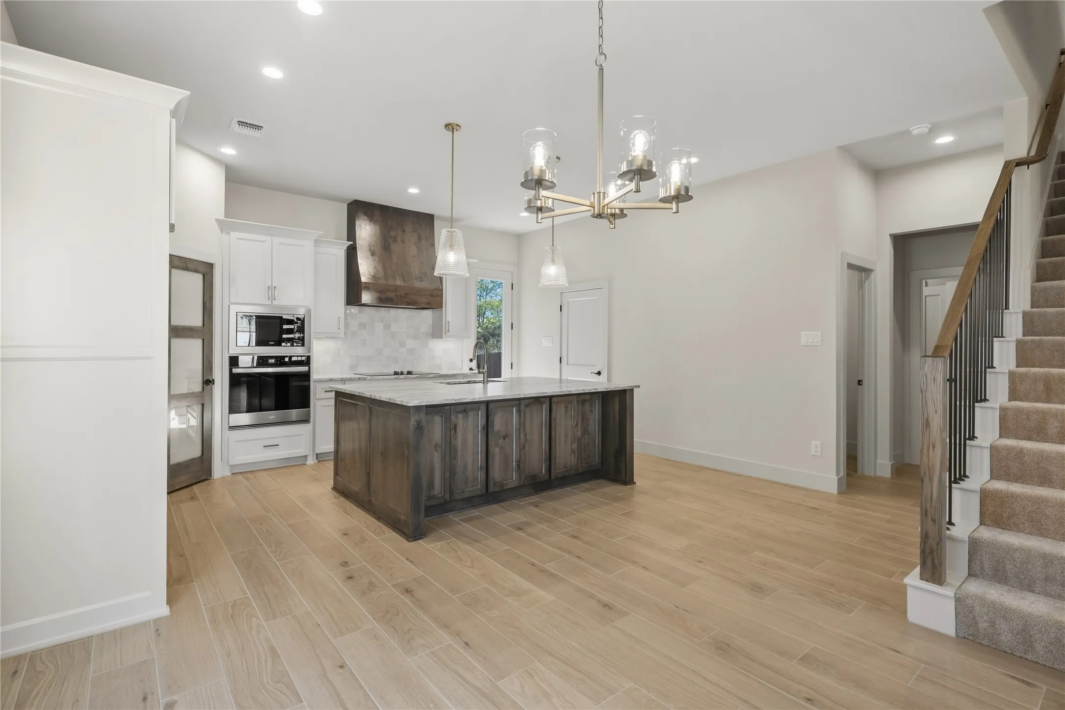 Open-concept kitchen featuring an island with a light-toned countertop, white cabinetry with integrated stainless steel appliances, a tile backsplash, and wood-finish flooring