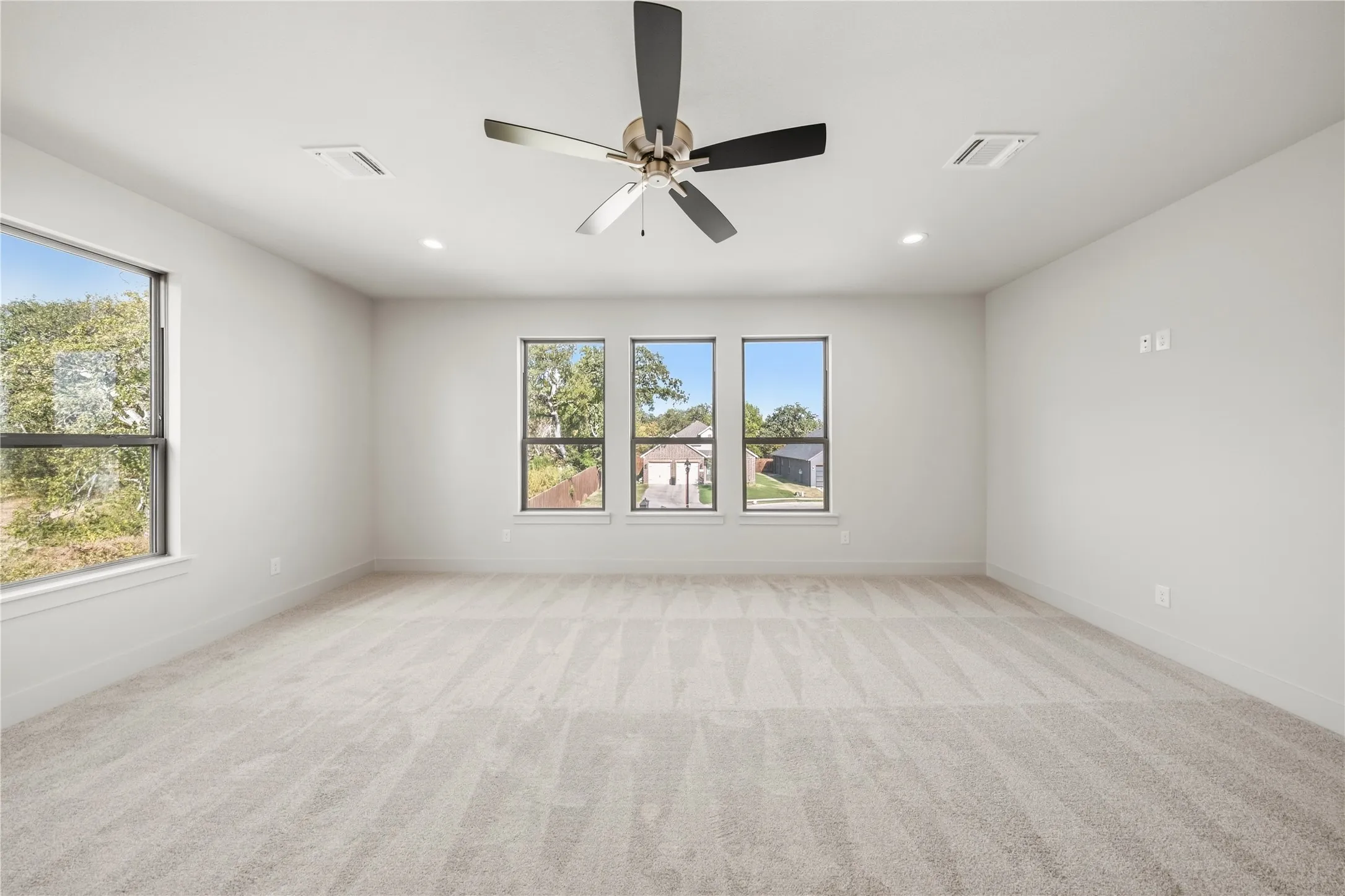 Spacious room with light-toned carpet, recessed lighting, and a contemporary ceiling fan