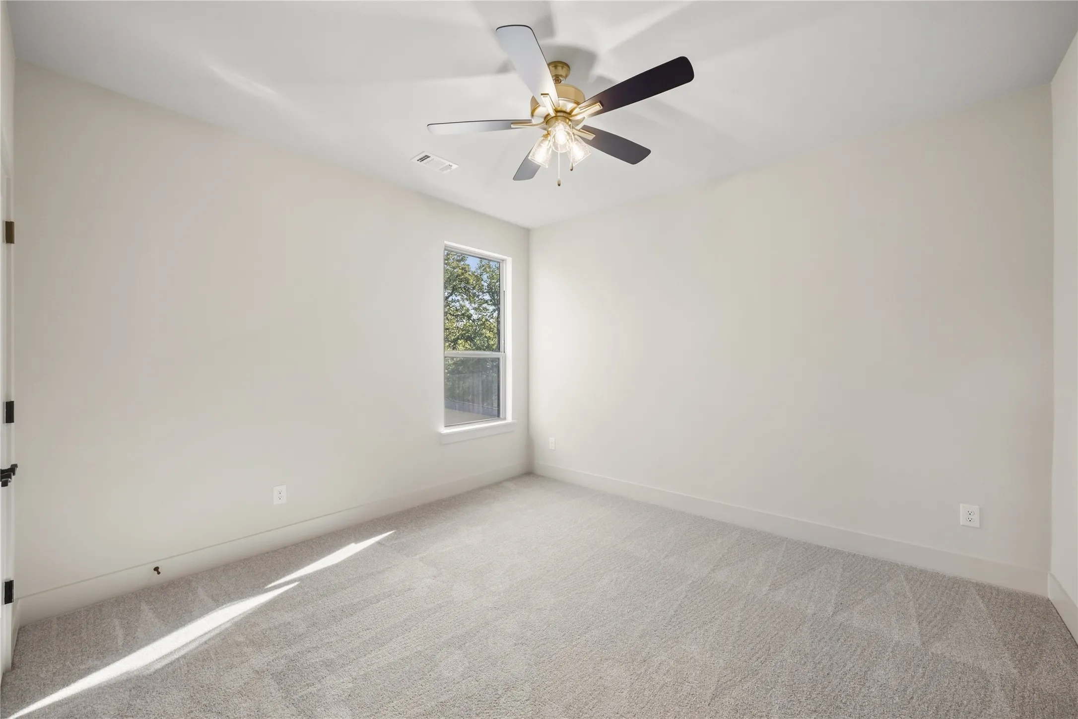 Bright bedroom with natural light from large window, neutral wall finishes, plush carpeting, and ceiling fan with integrated lighting fixture