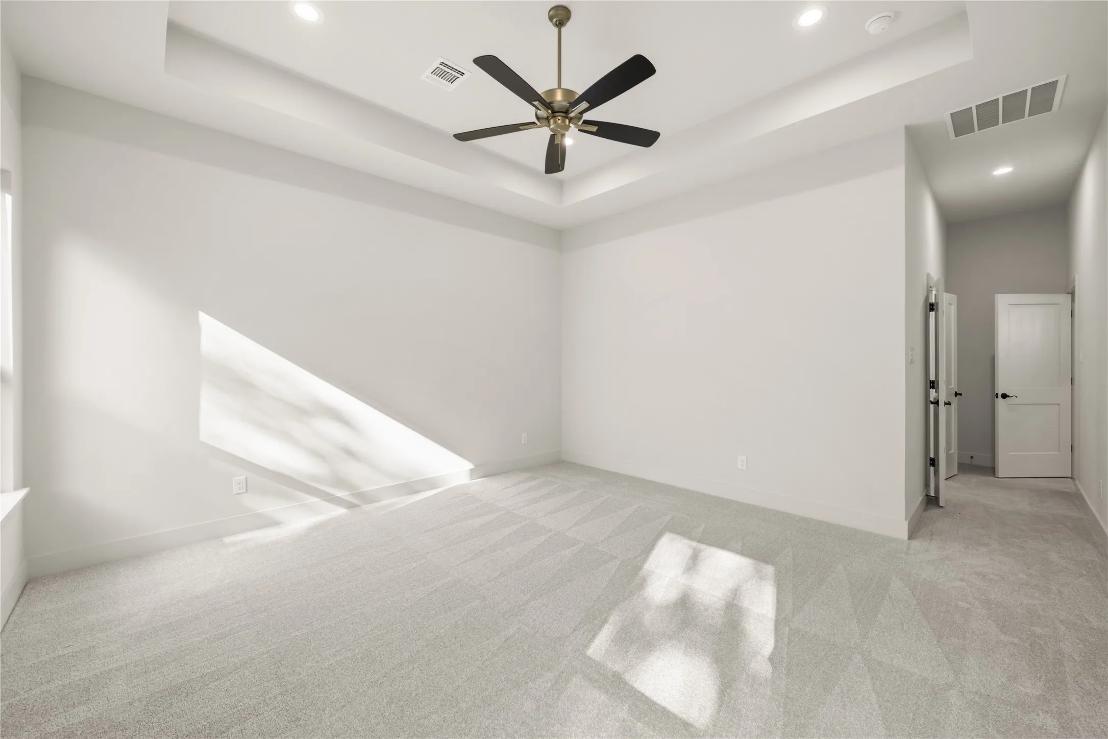Recessed lighting, tray ceiling with a built-in ceiling fan, light-toned carpeting, and a double-door closet entry