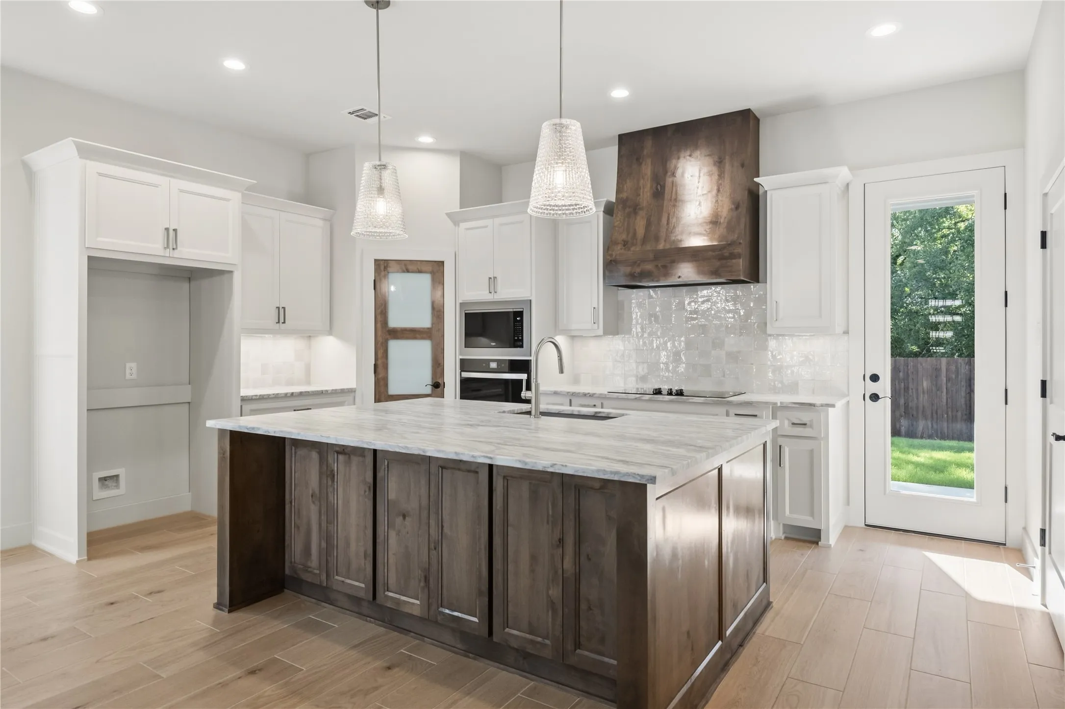 Gourmet kitchen featuring a wood-finish island, light-toned wood-finish flooring, white cabinetry, integrated stainless steel appliances, and a unique wood-finish range hood