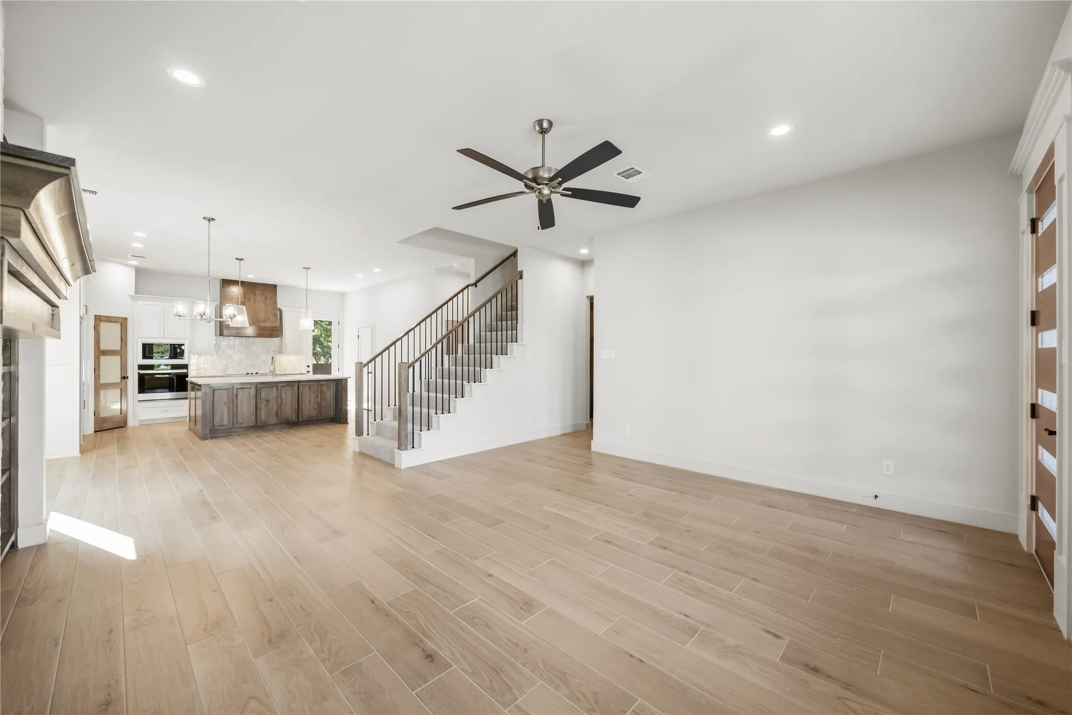 Wood-finish flooring, recessed lighting, and a contemporary ceiling fan define this expansive living space