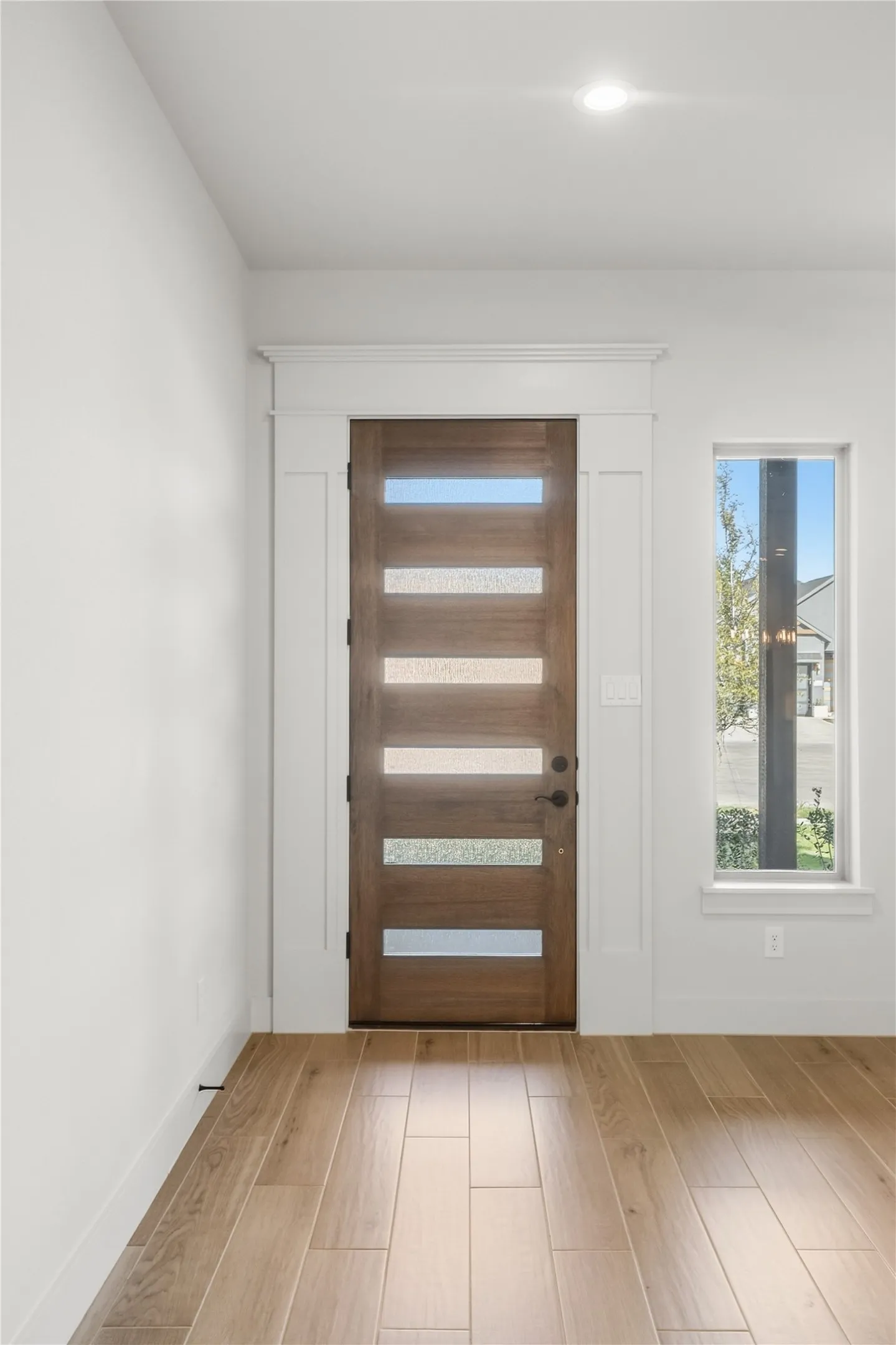 Contemporary wood-finish entry door with frosted glass panels, surrounded by white trim