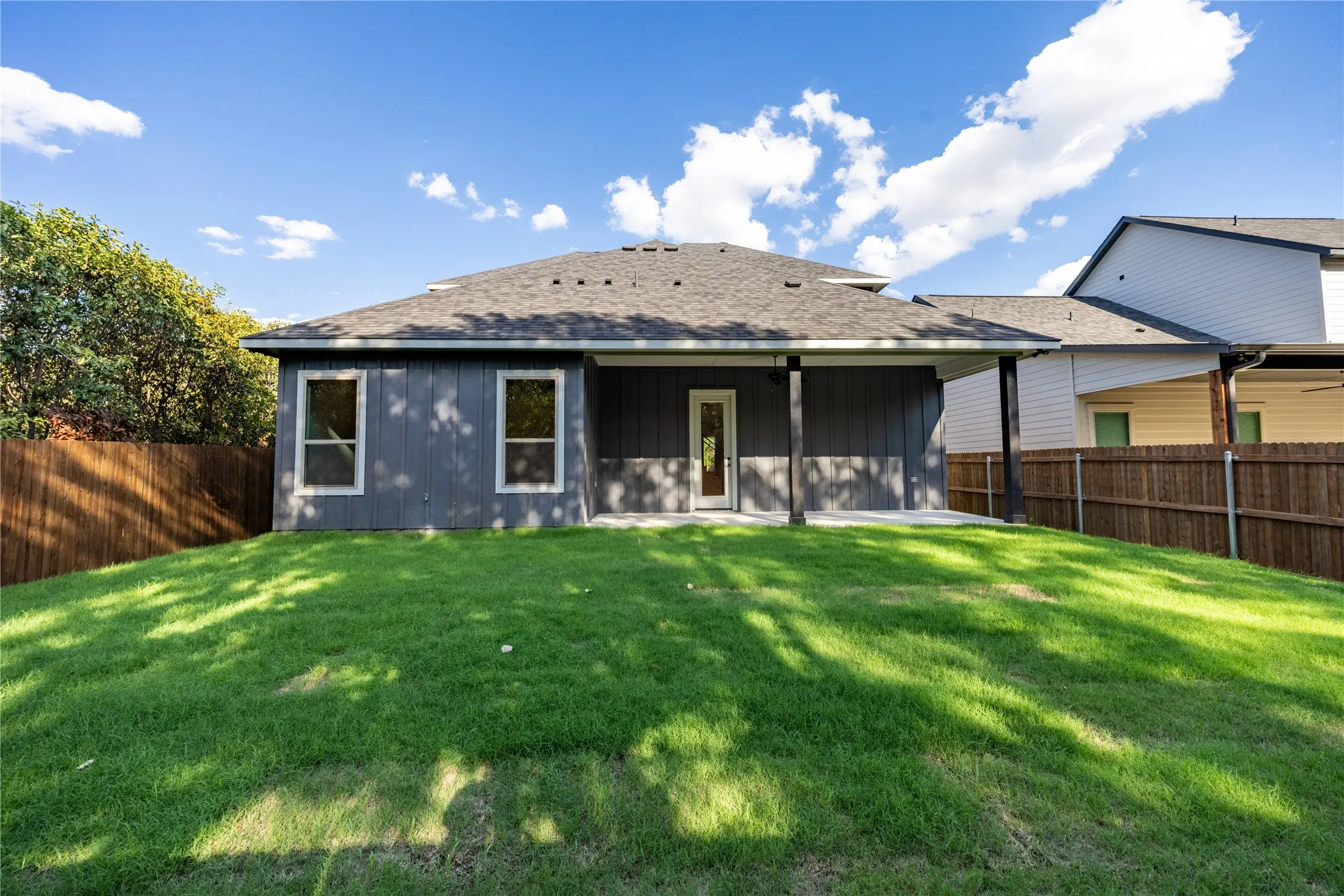 Expansive rear yard featuring a covered patio, wood privacy fencing, and a shingled roof