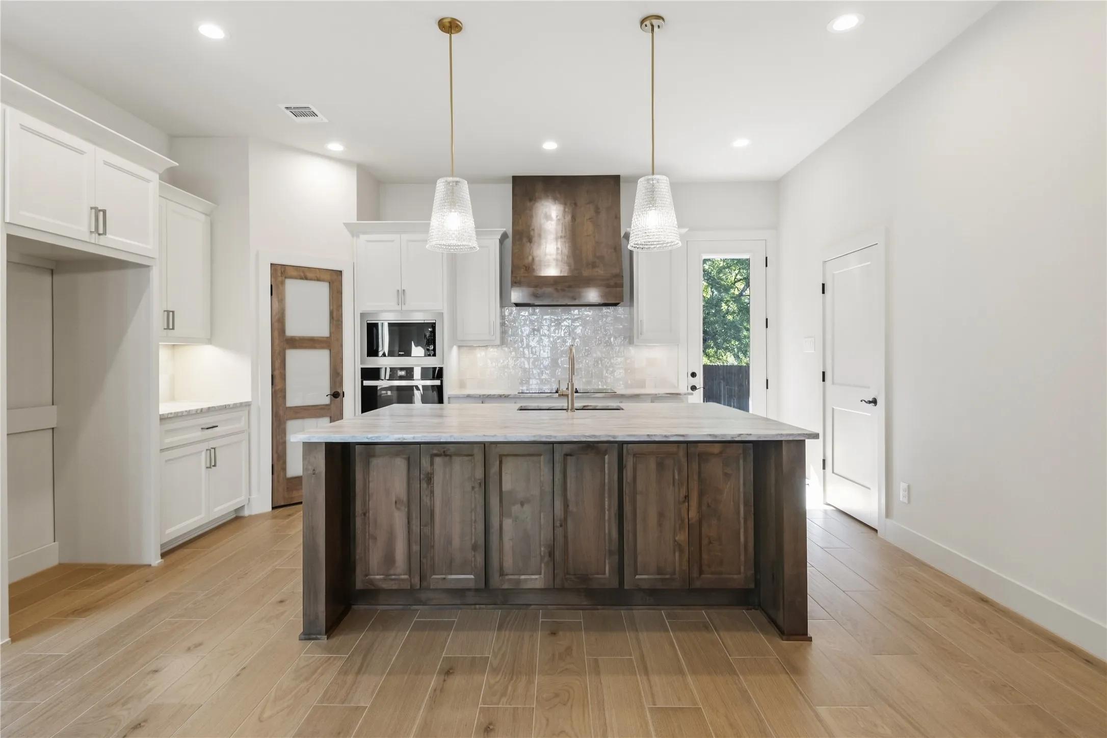 Spacious kitchen with a central island, white cabinetry, integrated stainless steel appliances, wood-finish flooring, and two pendant light fixtures