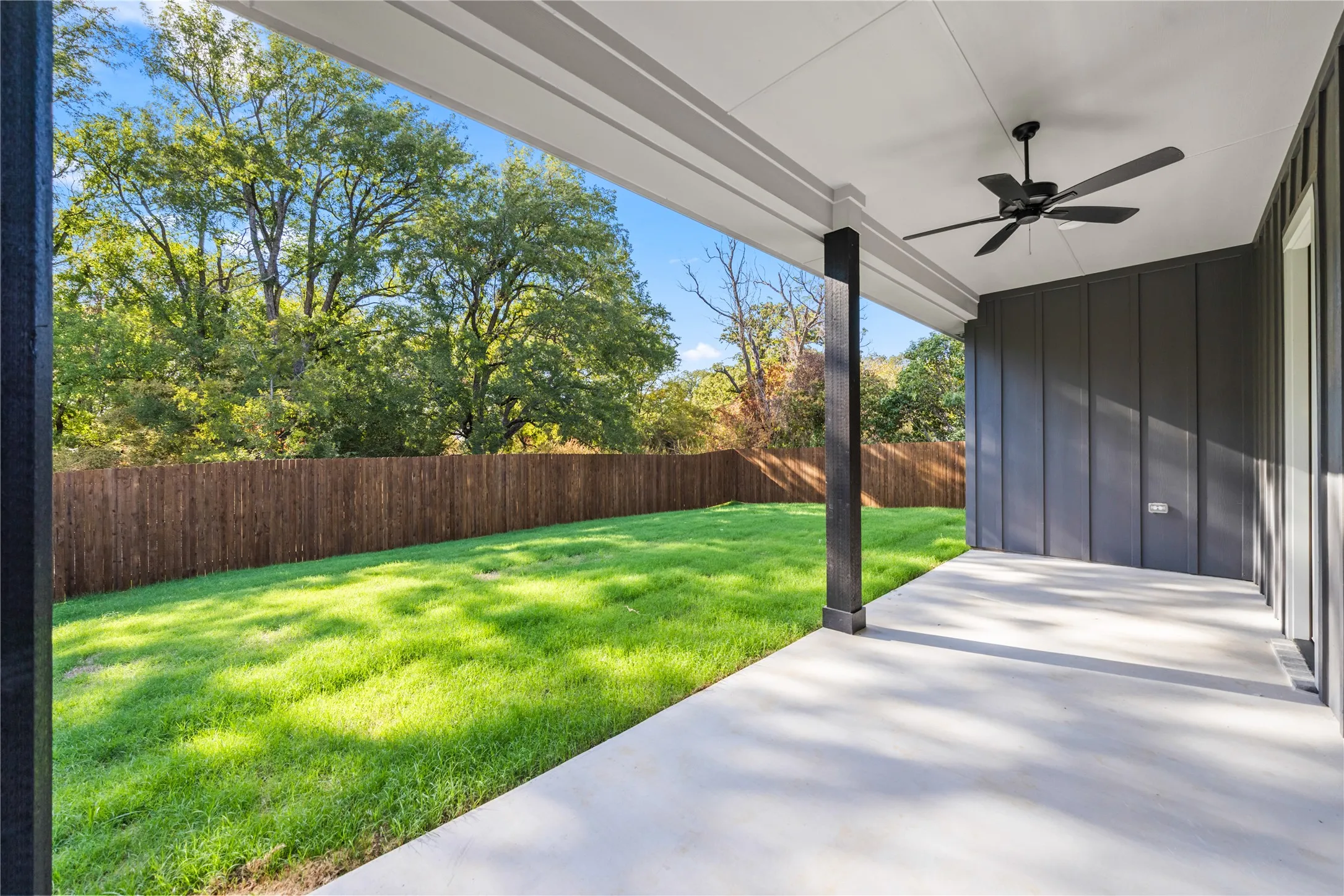 Covered patio with concrete flooring, black ceiling fan, and board and batten siding